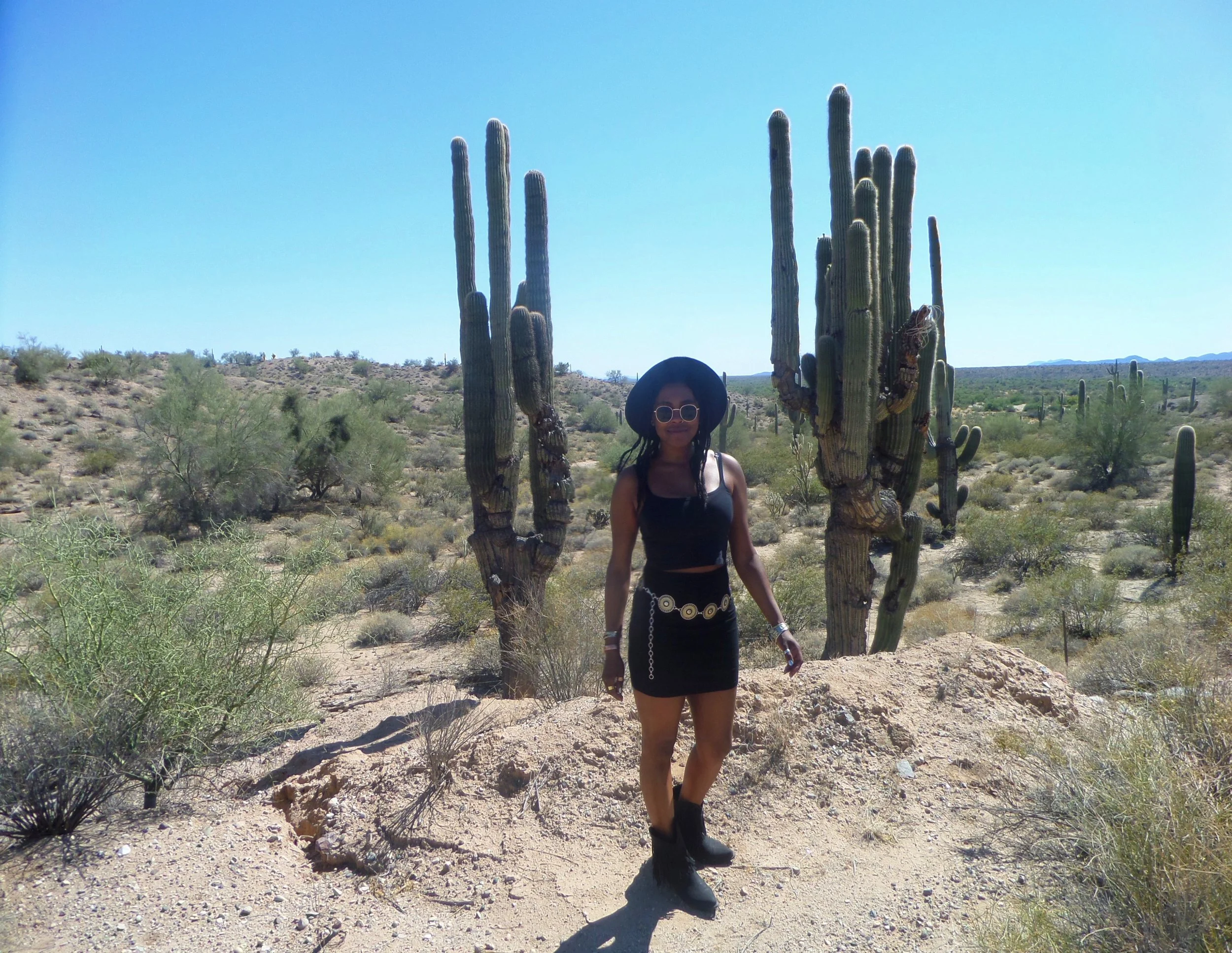 Woman standing in the Arizona desert surrounded by tall saguaro cacti on the road to Wickenburg.