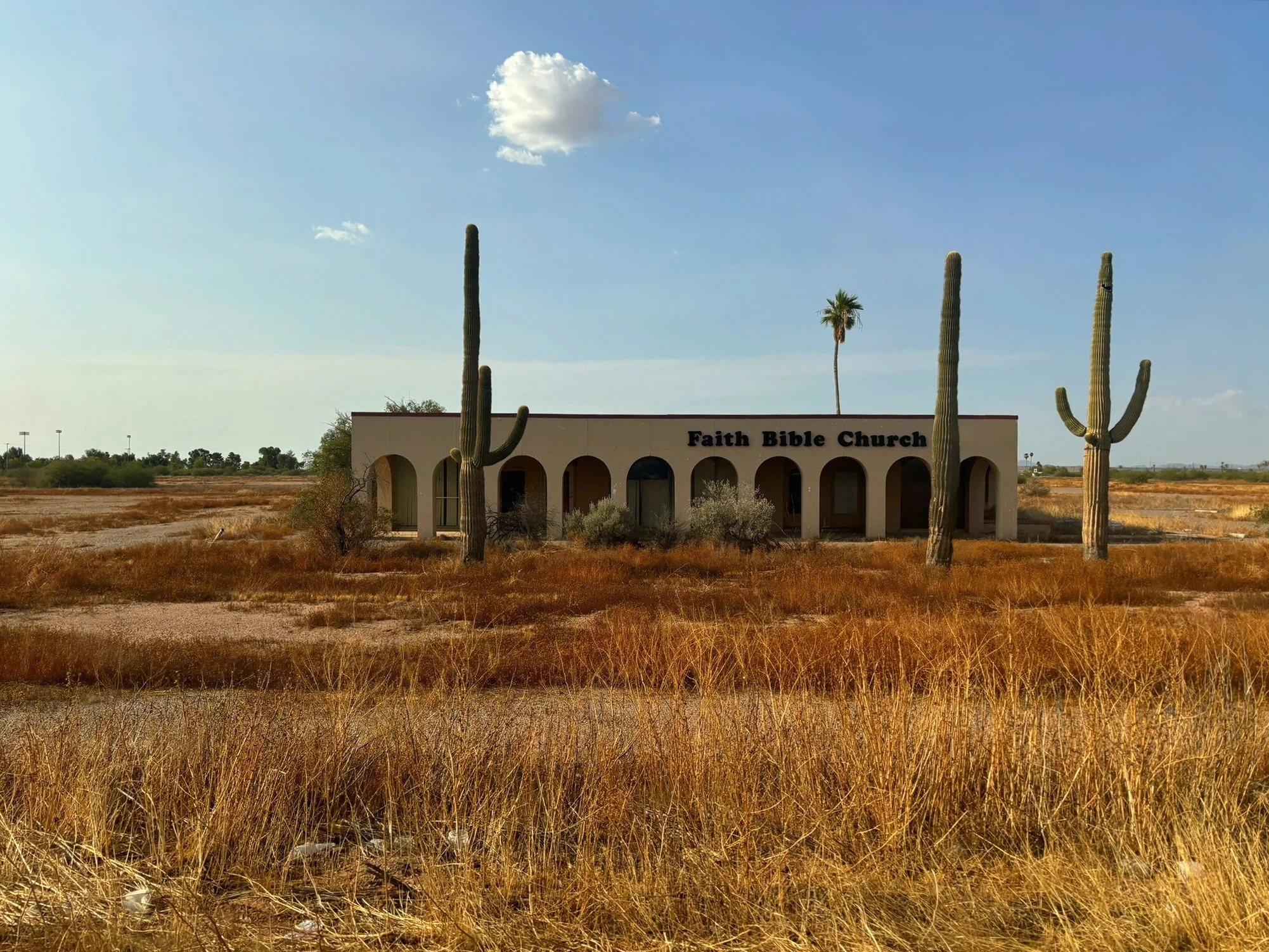 Abandoned Faith Bible Church surrounded by towering saguaro cacti along Highway 84 near Stanfield, Arizona.
