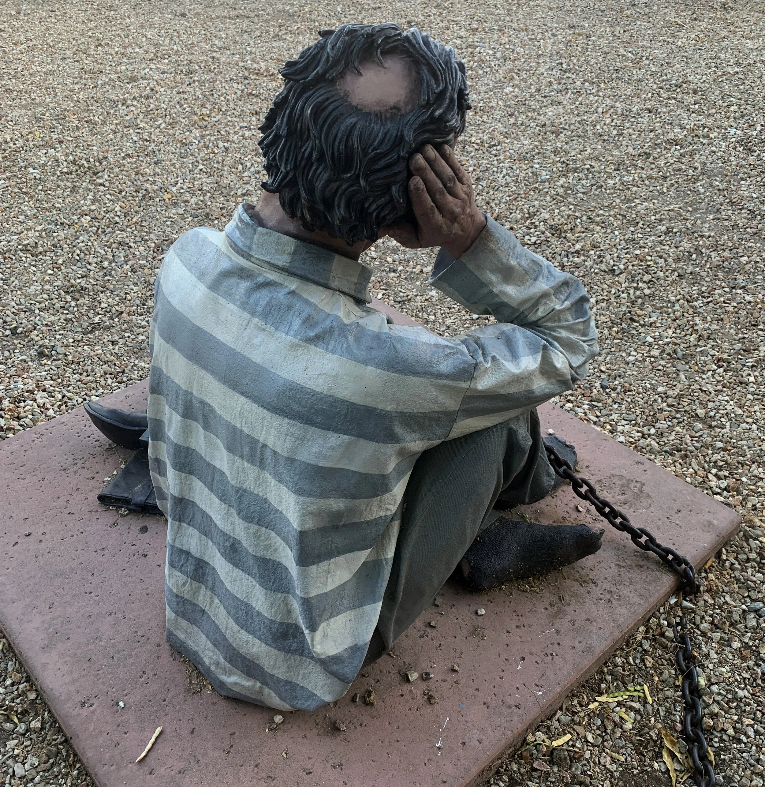 Back view of the chained prisoner statue at the historic Wickenburg Jail Tree site in Arizona.