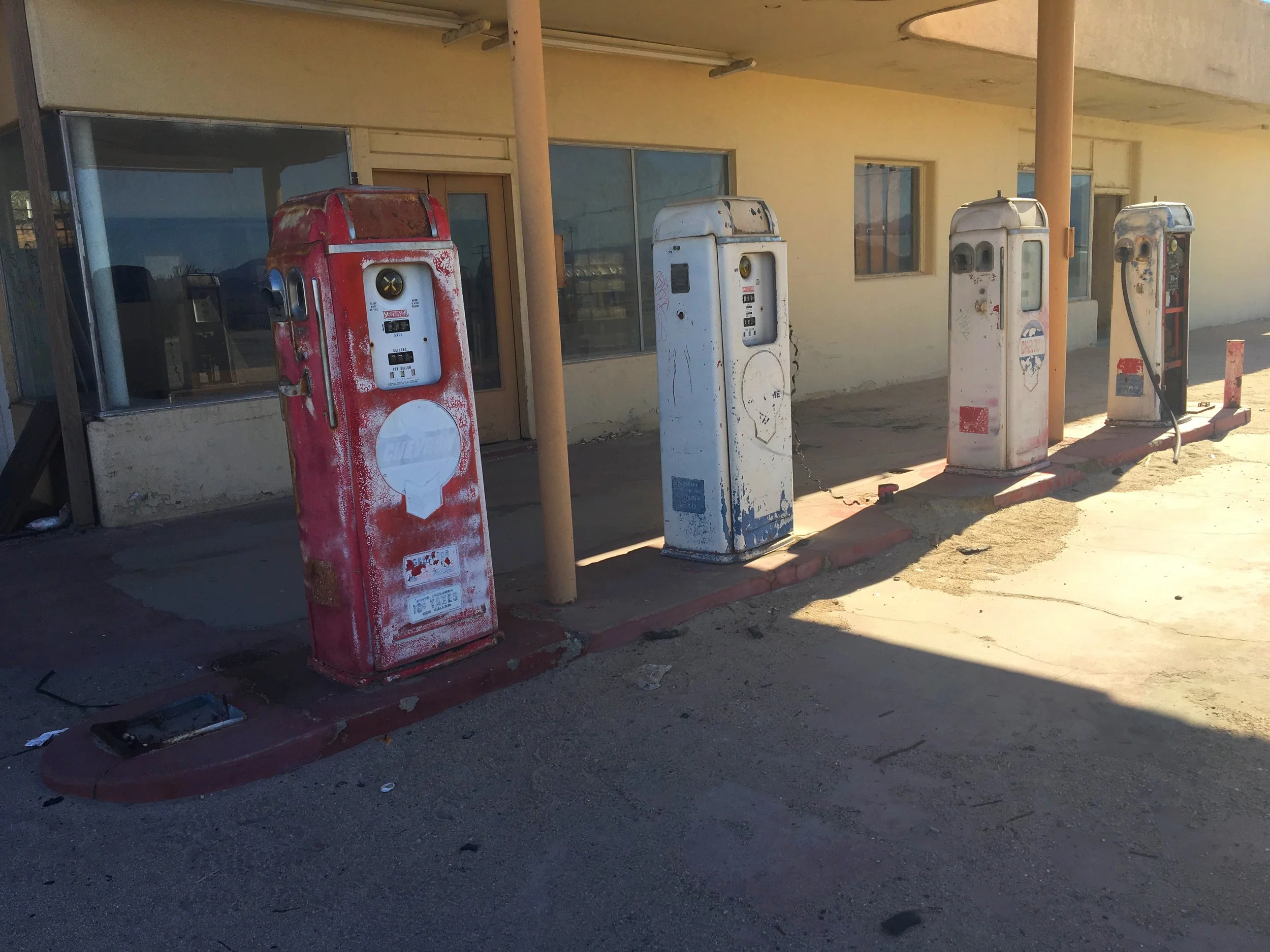 Row of weathered vintage gas pumps outside an abandoned desert service station.