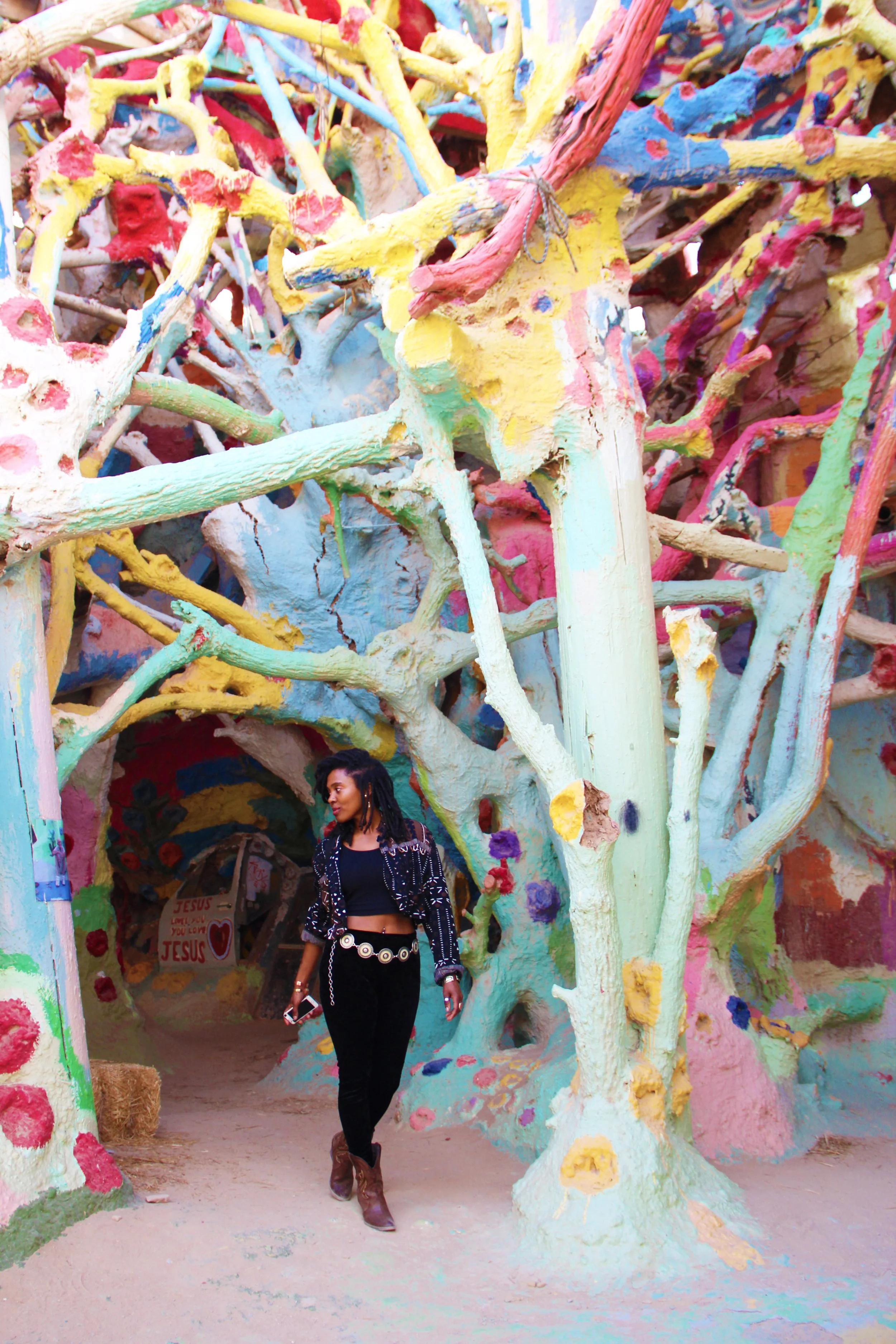 Visitor walking beneath a maze of brightly painted branches and recycled wood sculptures at East Jesus in Slab City, California.