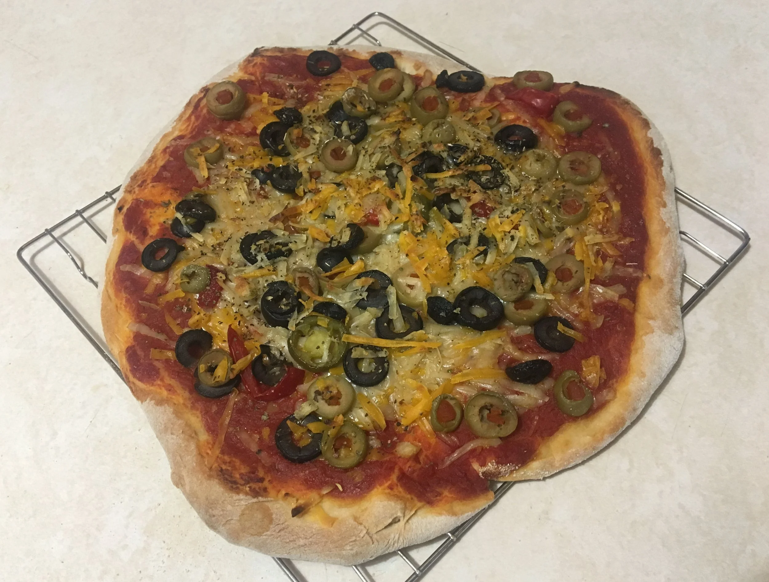 Homemade vegan pizza topped with vegan cheese, black olives, and sliced jalapeños.