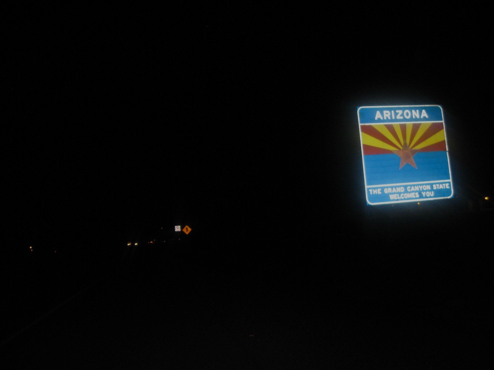 Nighttime road sign welcoming travelers to Arizona with the state flag and text.