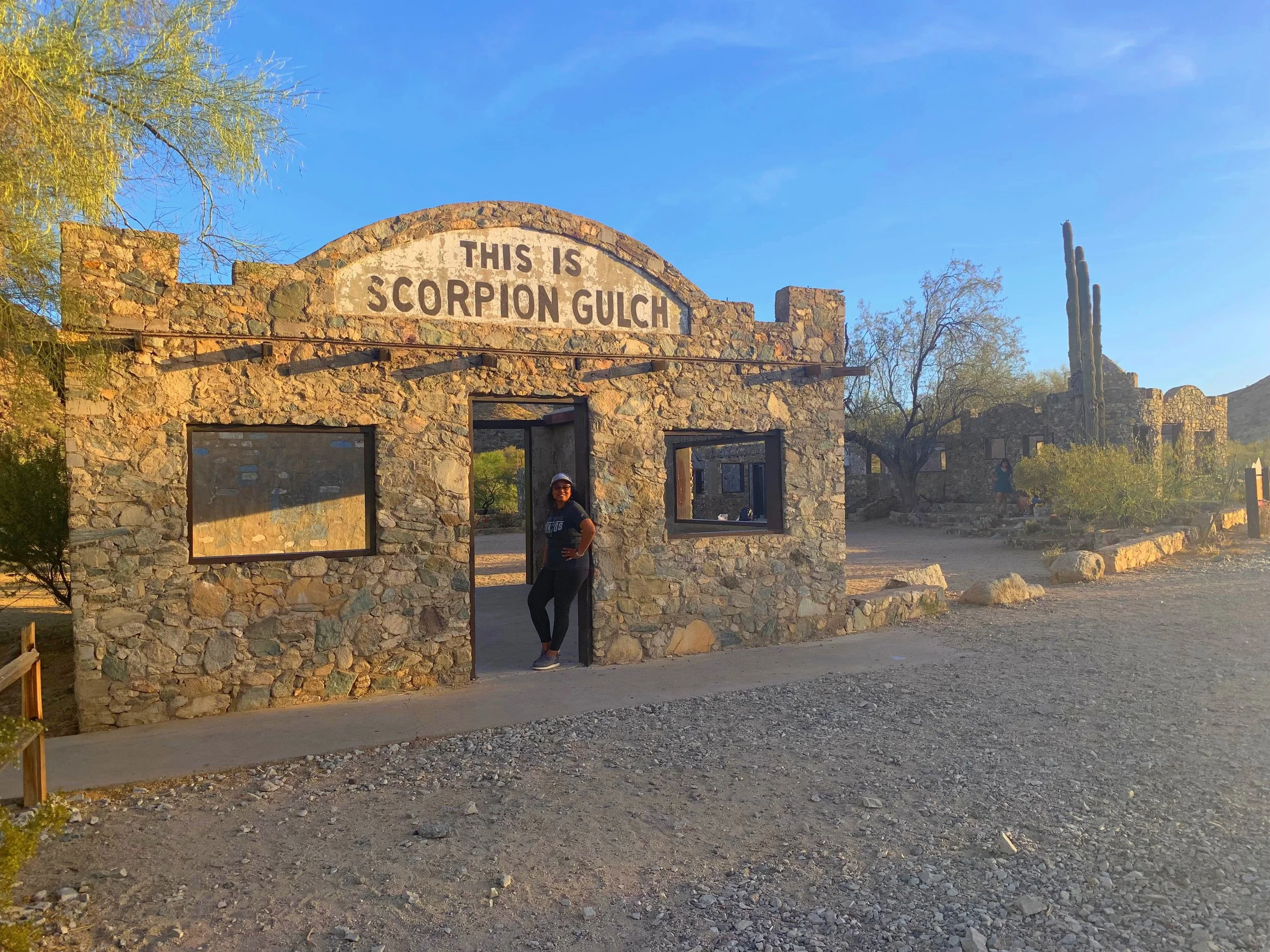 Historic Scorpion Gulch stone entrance with its painted sign and the tall aging saguaro visible beside the ruins in 2022.