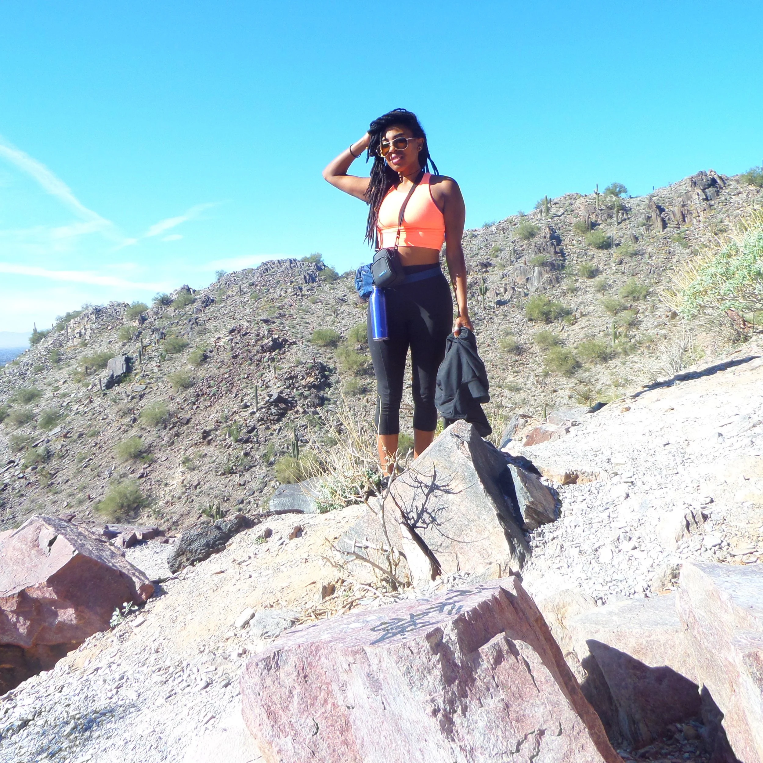 Hiker standing on the rocky slopes of Piestewa Peak surrounded by Sonoran Desert terrain and saguaros.