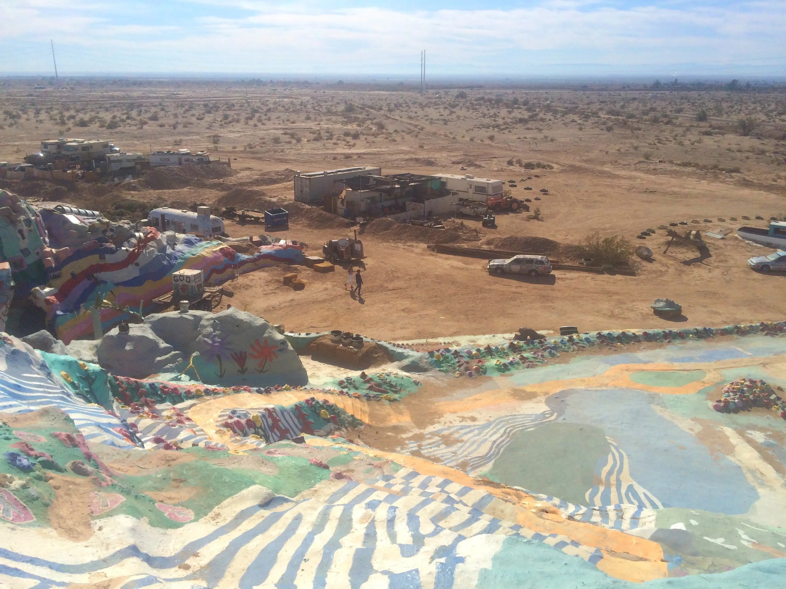 Panoramic view from Salvation Mountain showing nearby desert structures, vehicles, and open landscape.