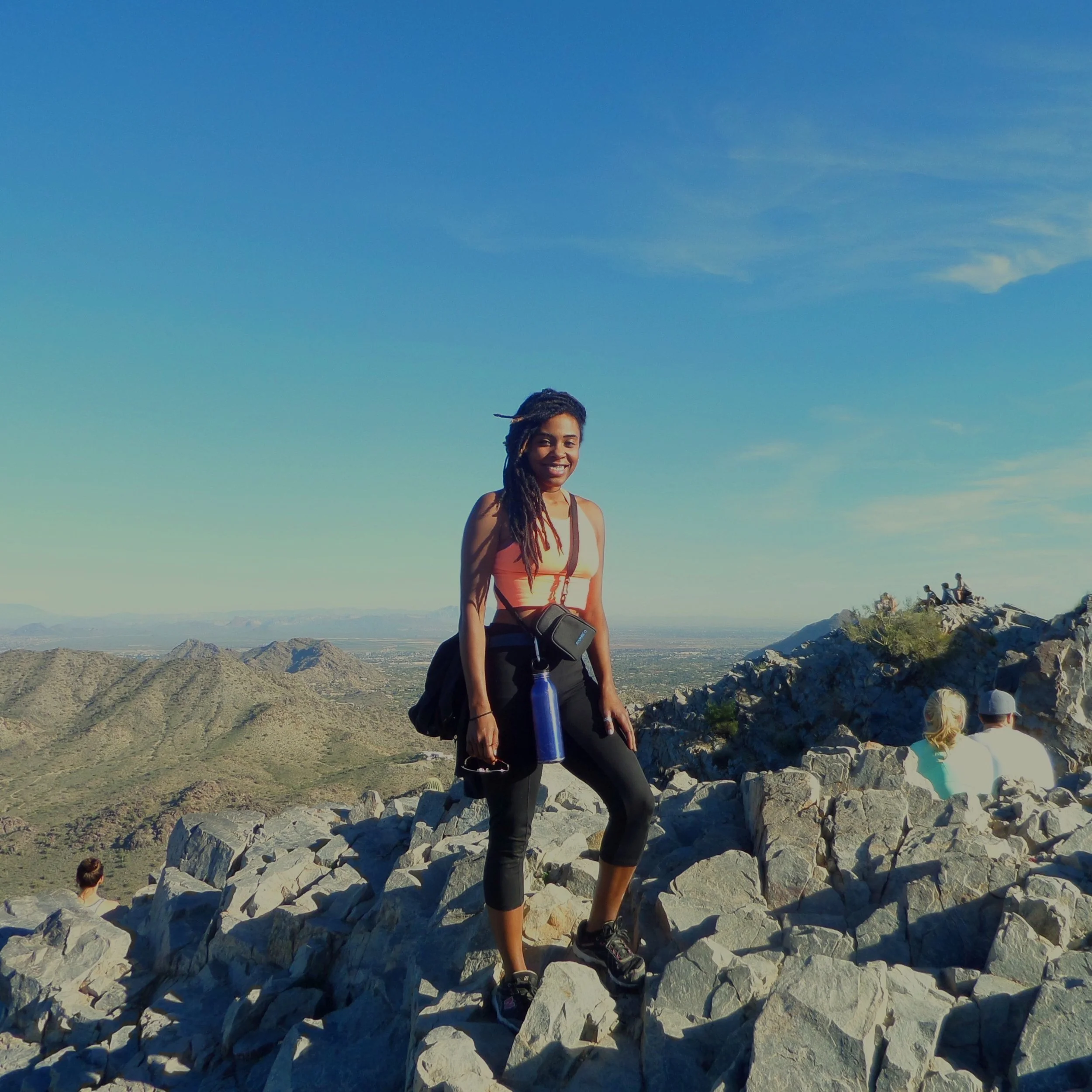 Hiker standing on the rocky summit of Piestewa Peak with desert mountains in the background.