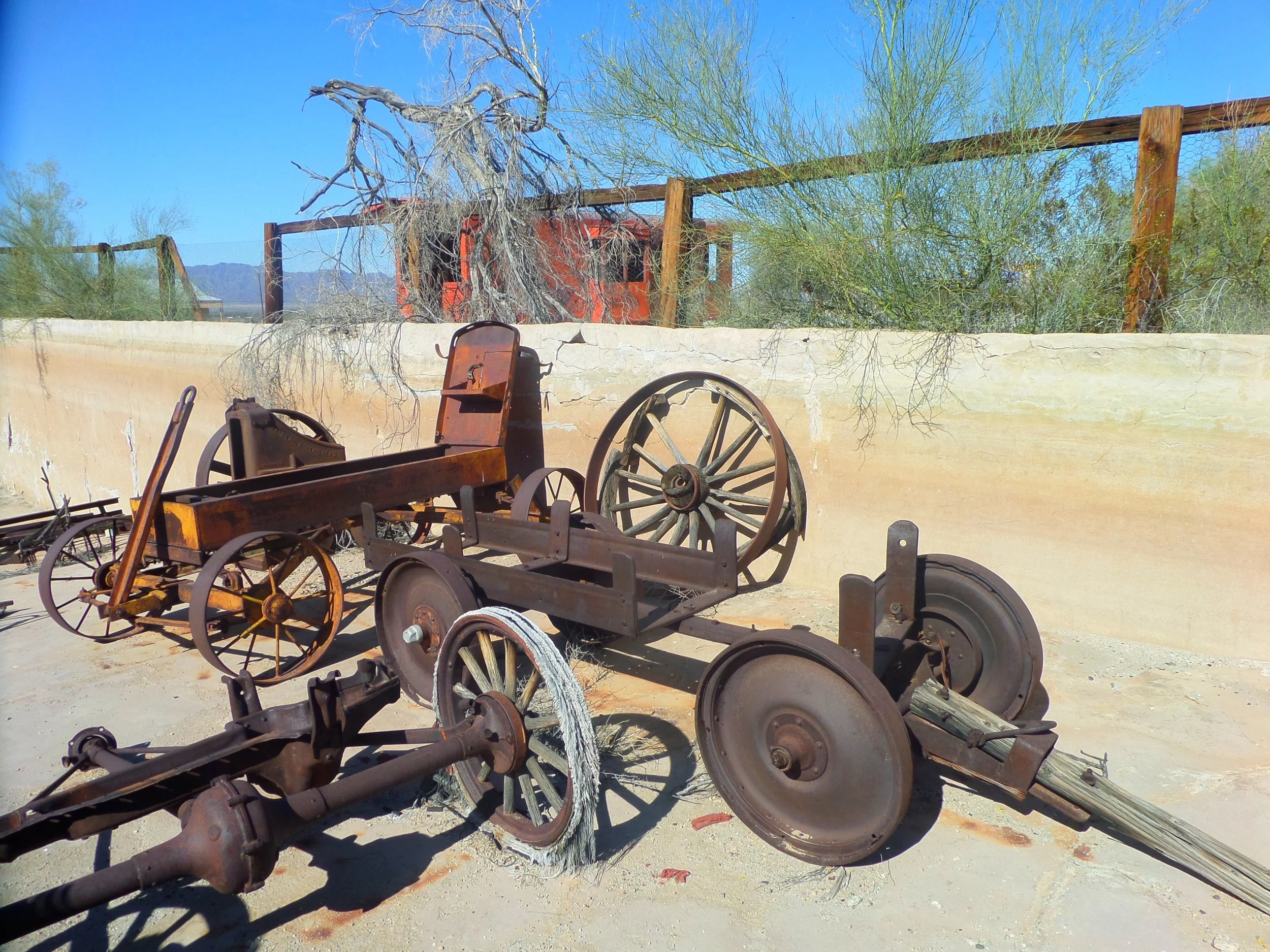 Rusted antique wagon frame preserved in an outdoor desert exhibit.