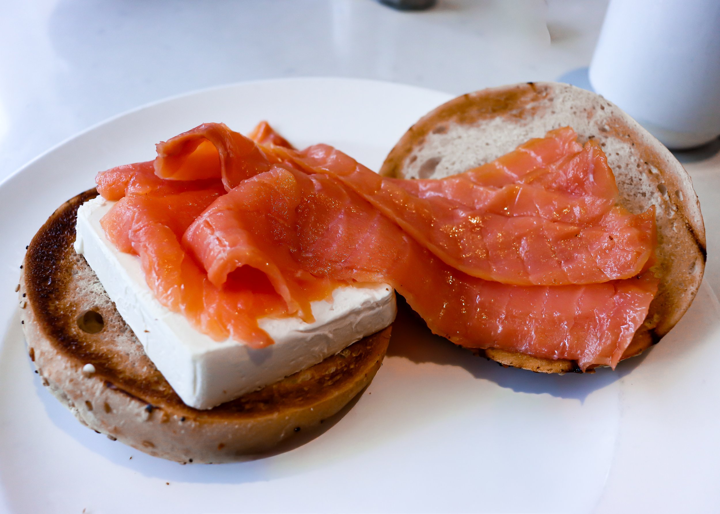 Bagel half with cream cheese and smoked salmon on top, served on a white plate.