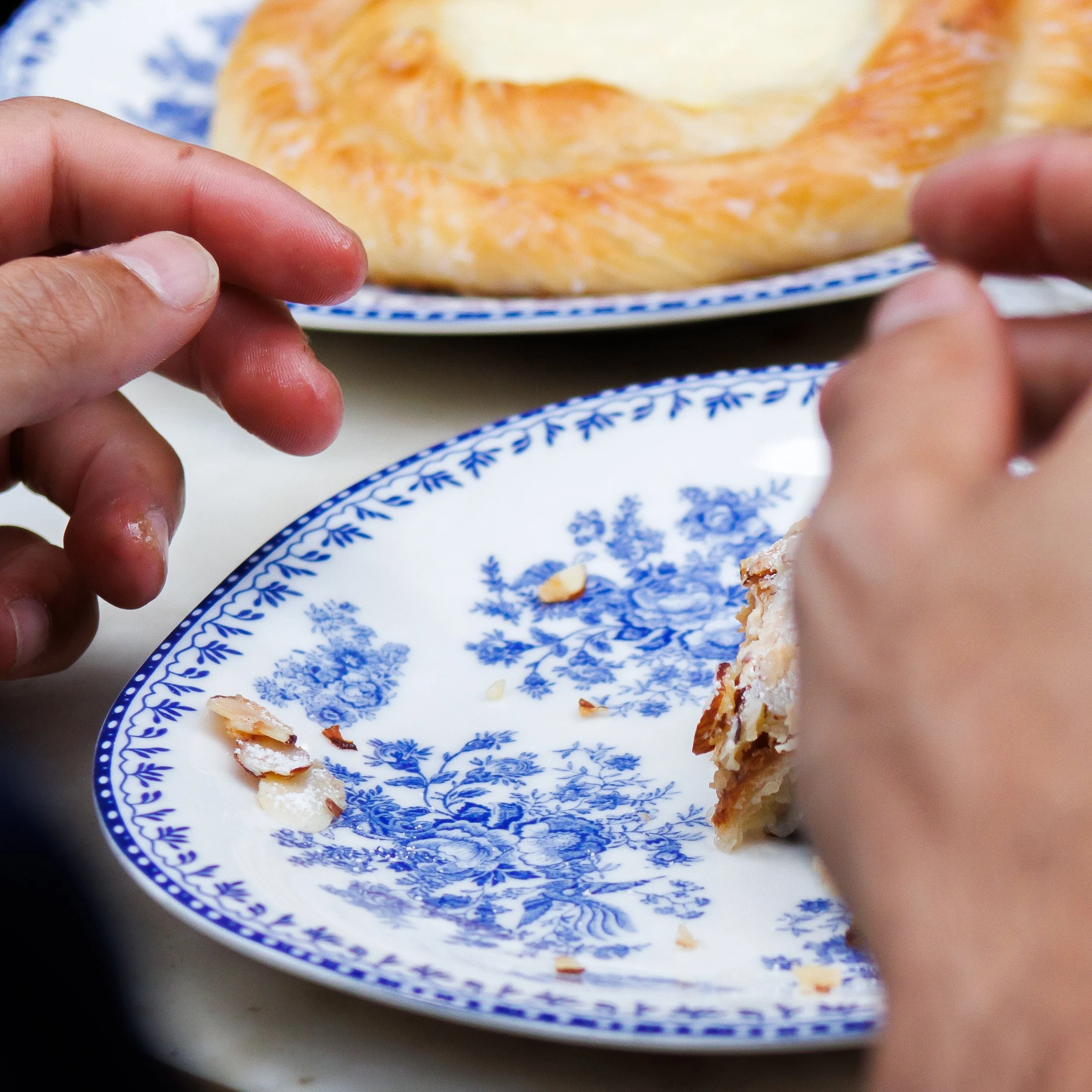 Person eating a slice of pie with a dollop of whipped cream on a blue and white floral plate.