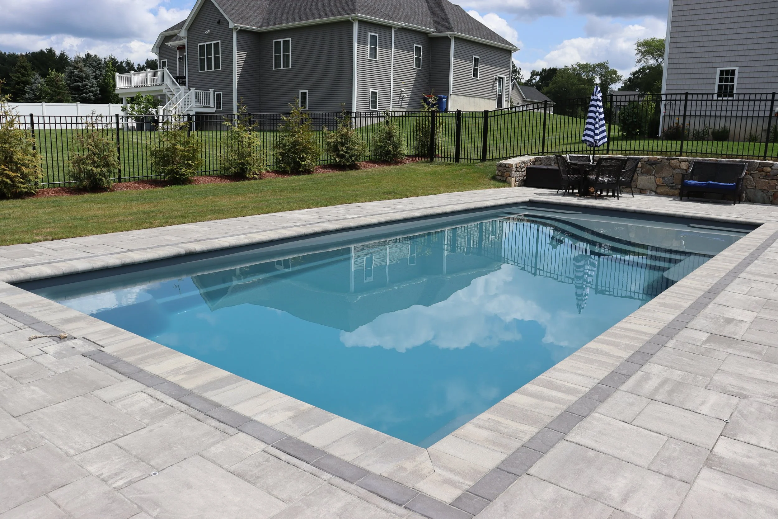 Backyard with in-ground swimming pool, patio area, and houses in background.