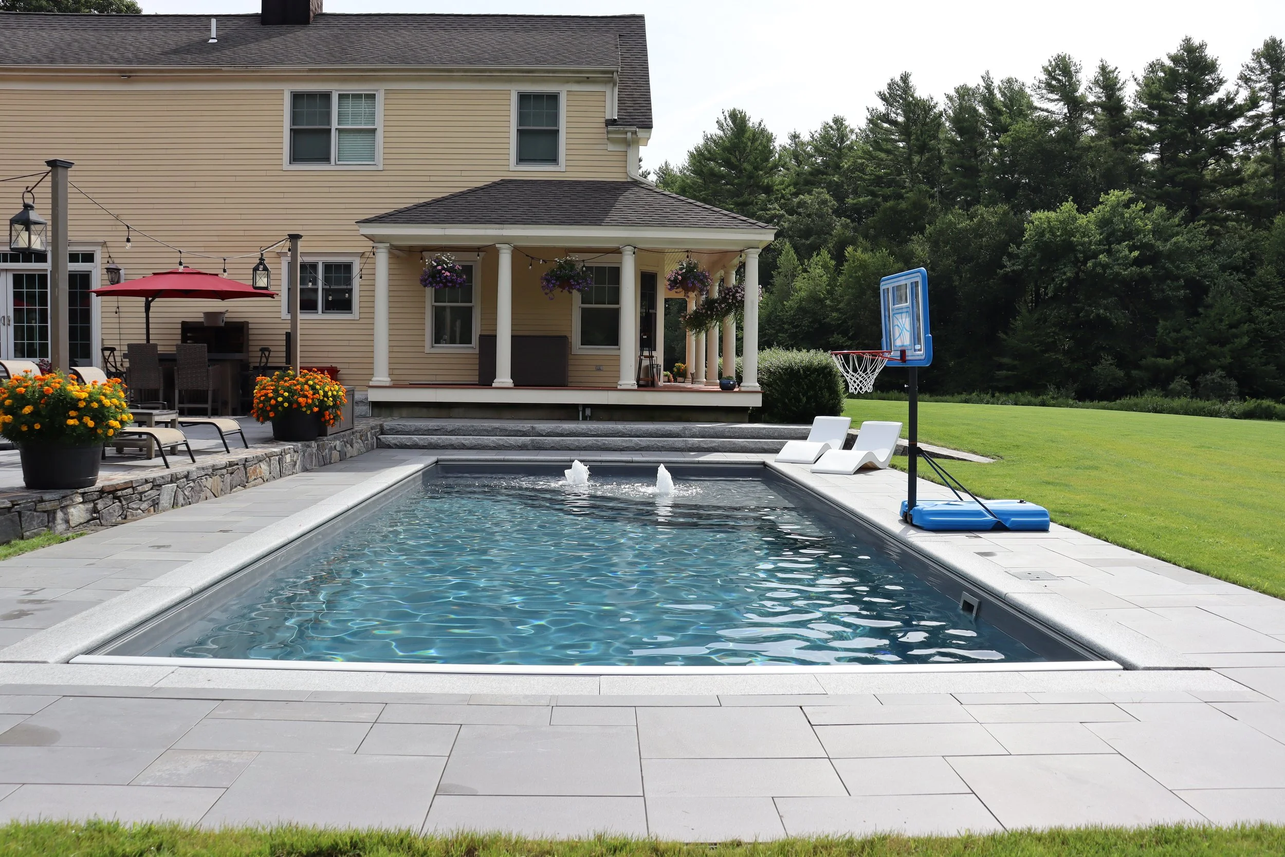 Backyard with swimming pool, lounge chairs, and a basketball hoop in the yard.