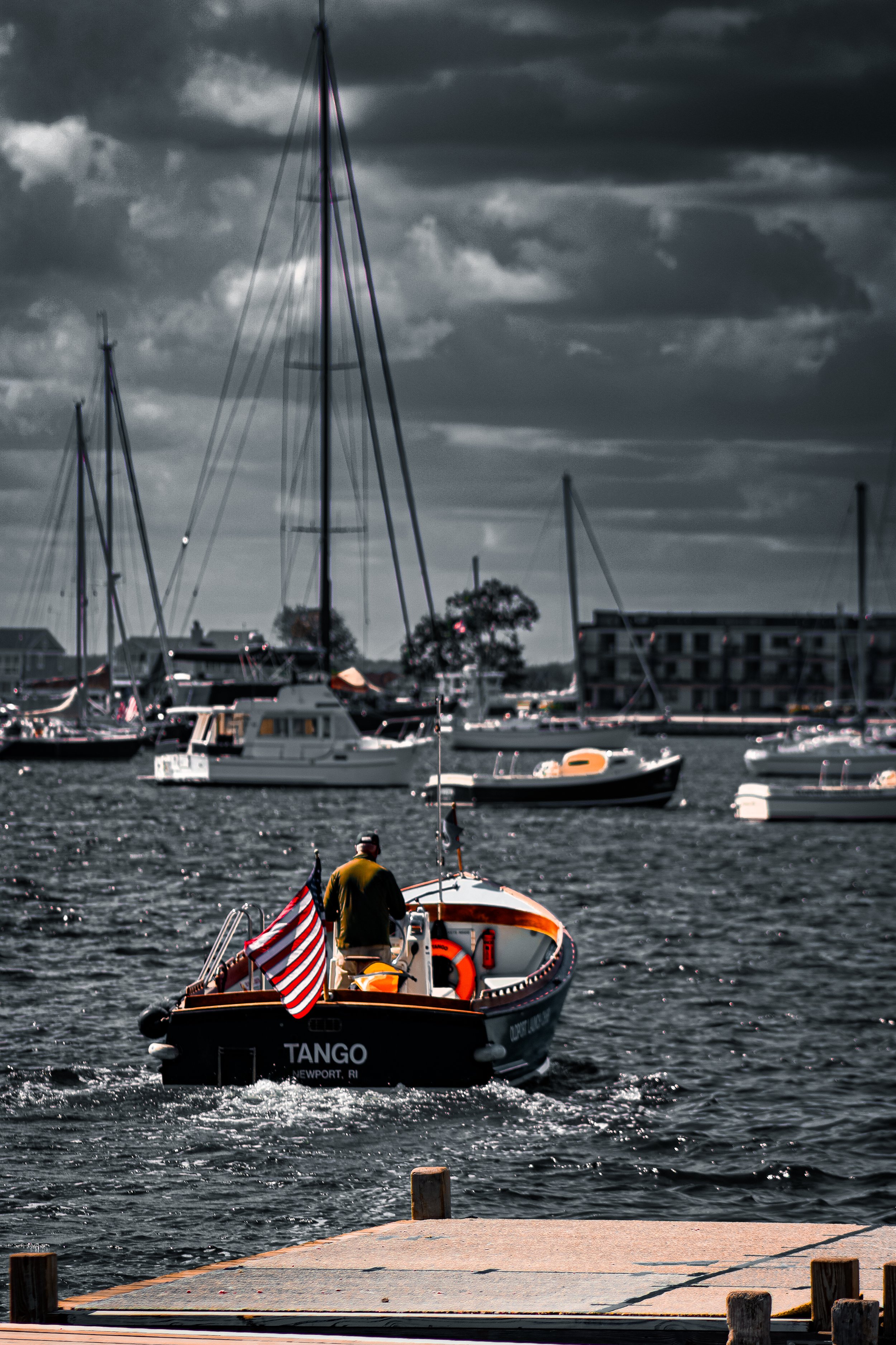 A boat named 'TANGO' on the water in a marina with multiple sailboats and motorboats, buildings and cloudy sky in the background.