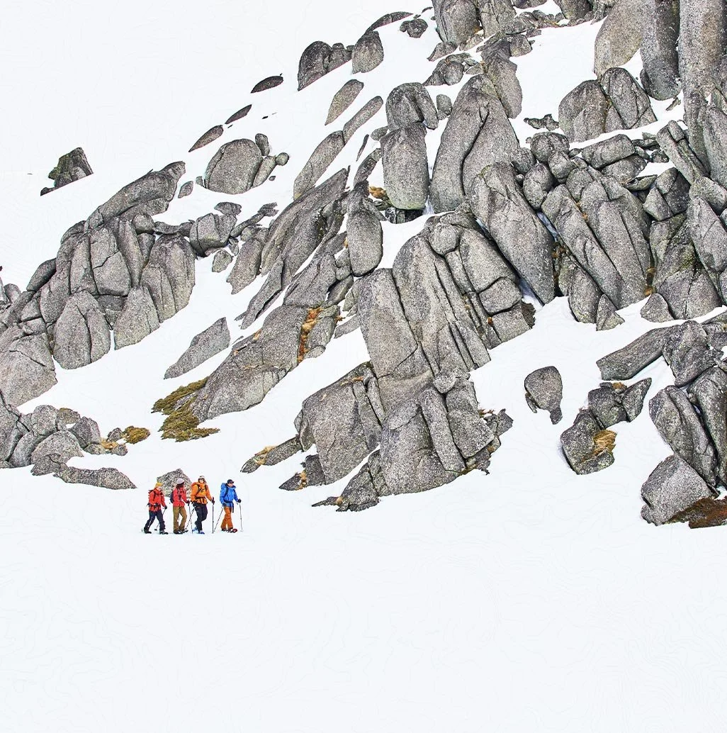 A group of hikers navigate the snow-covered terrain amidst striking rock formations in Kosciuszko National Park, Snowy Mountains, NSW, Australia.