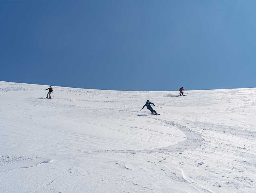 Three skiers on a Main Range slope under clear skies