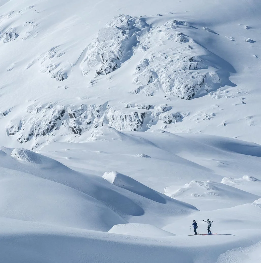 Two skiers traverse the expansive snowy landscape of Kosciuszko National Park in the Snowy Mountains, NSW, Australia, dwarfed by the stunning snow-covered peaks.