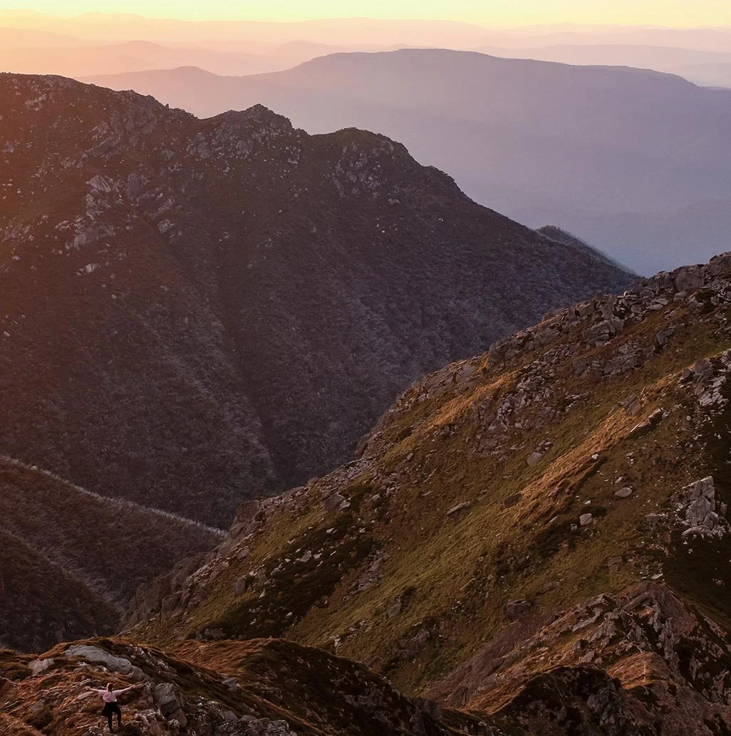 An adventurer stands atop the sunlit peaks of Kosciuszko National Park in Snowy Mountains, Australia.