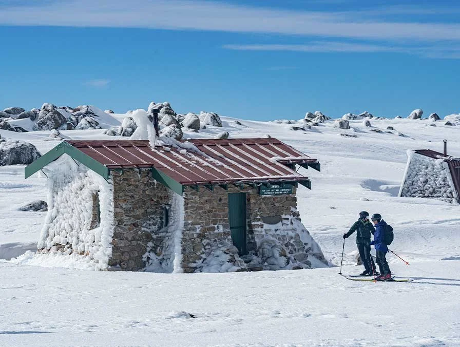 Skiing past a stone alpine shelter on the Main Range