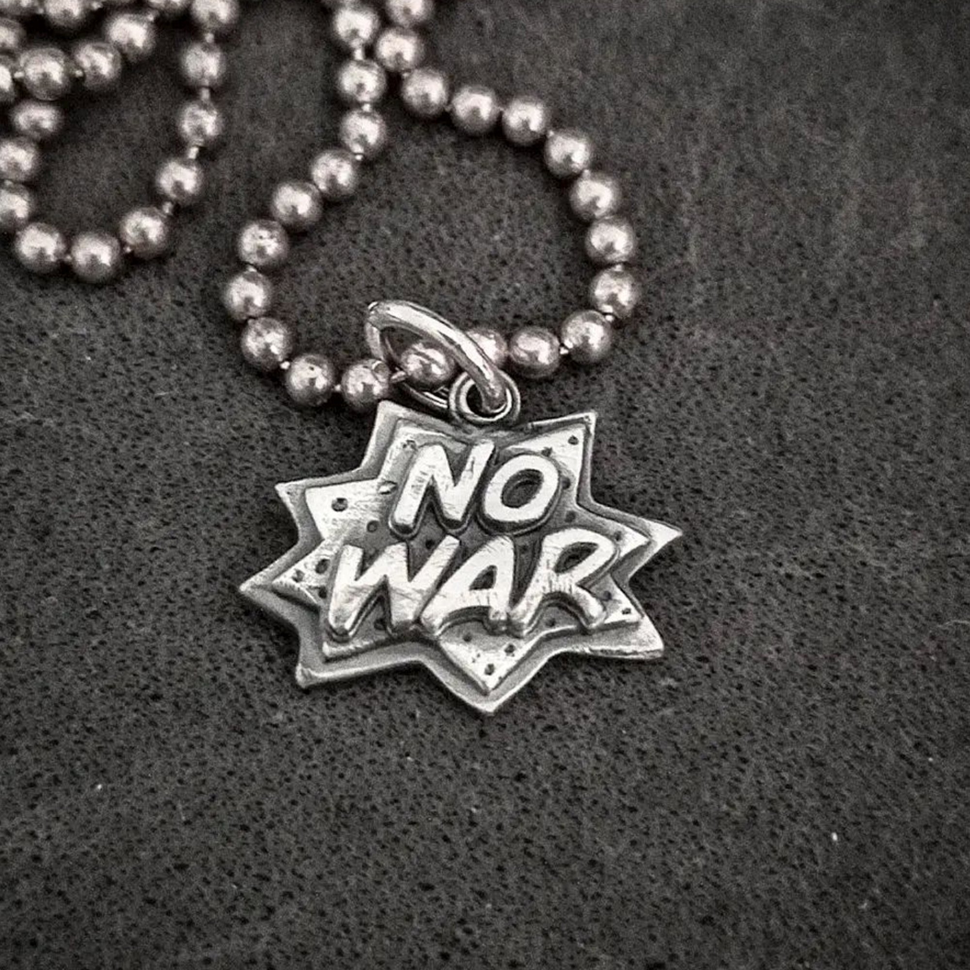 Pendant with "No War" text on a beaded chain.
