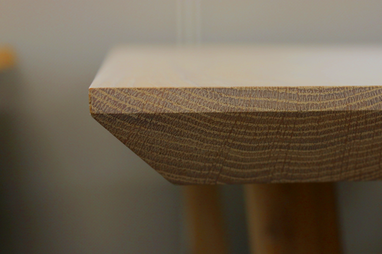 Close-up of the corner of a wooden table showing the textured edge and smooth surface.