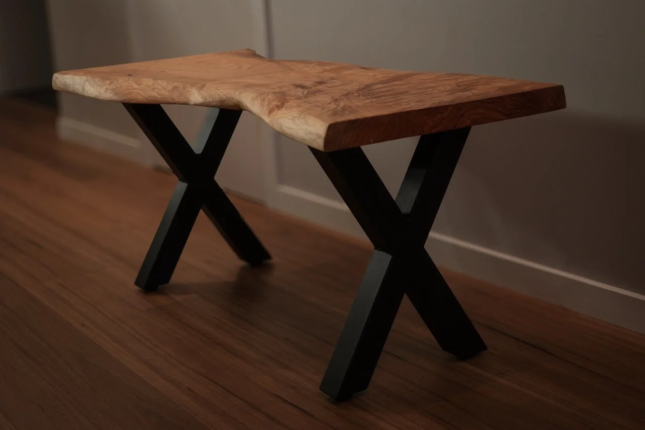Wide-angle shot of a custom live edge timber bench featuring a natural highly figured edge and sturdy black X-frame metal legs