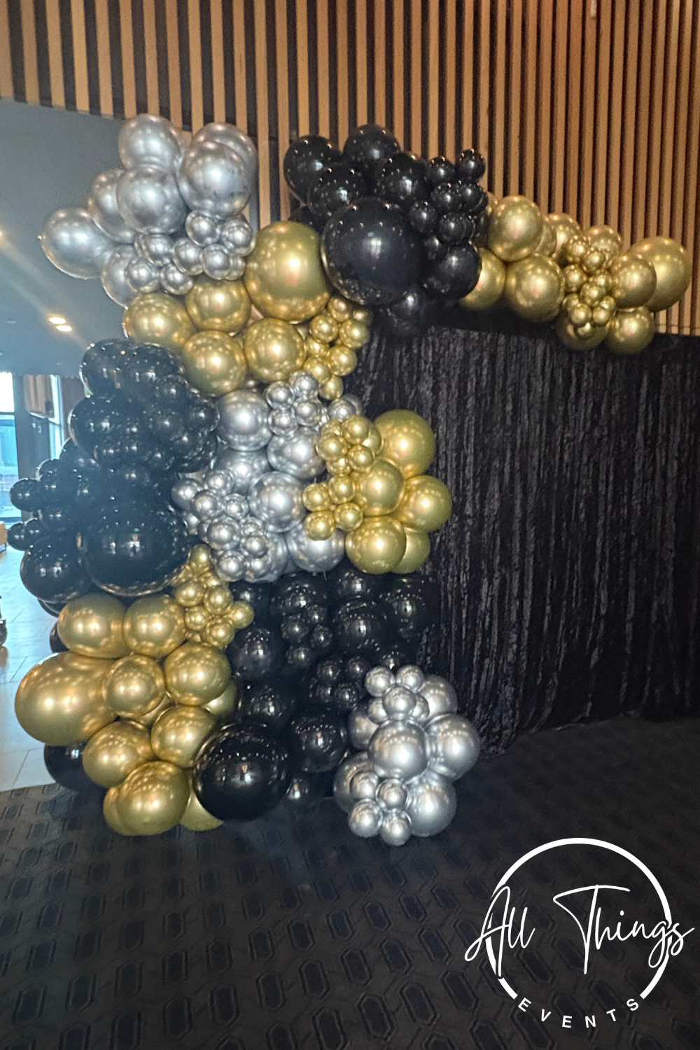 Decorative balloon arch with black, silver, and gold balloons at an event space.