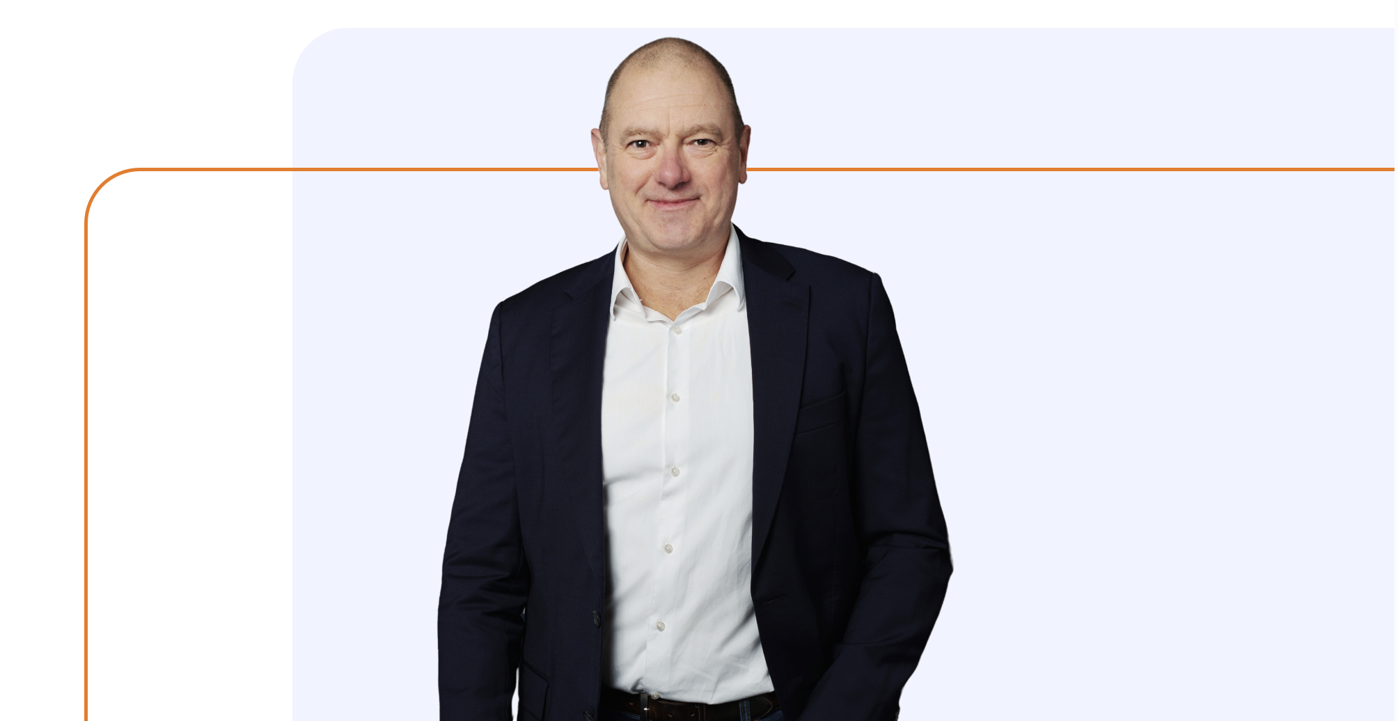 A portrait of a man with a bald head and light skin, wearing a white dress shirt and a black blazer, standing against a light background with a thin orange line.