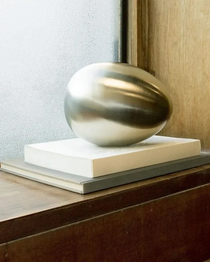 A metallic sculpture resembling an egg on a square white base, placed on top of two stacked books.