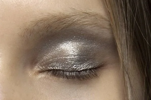 Close-up of a person's eye with closed eyelid, showcasing metallic silver eyeshadow on the eyelid.