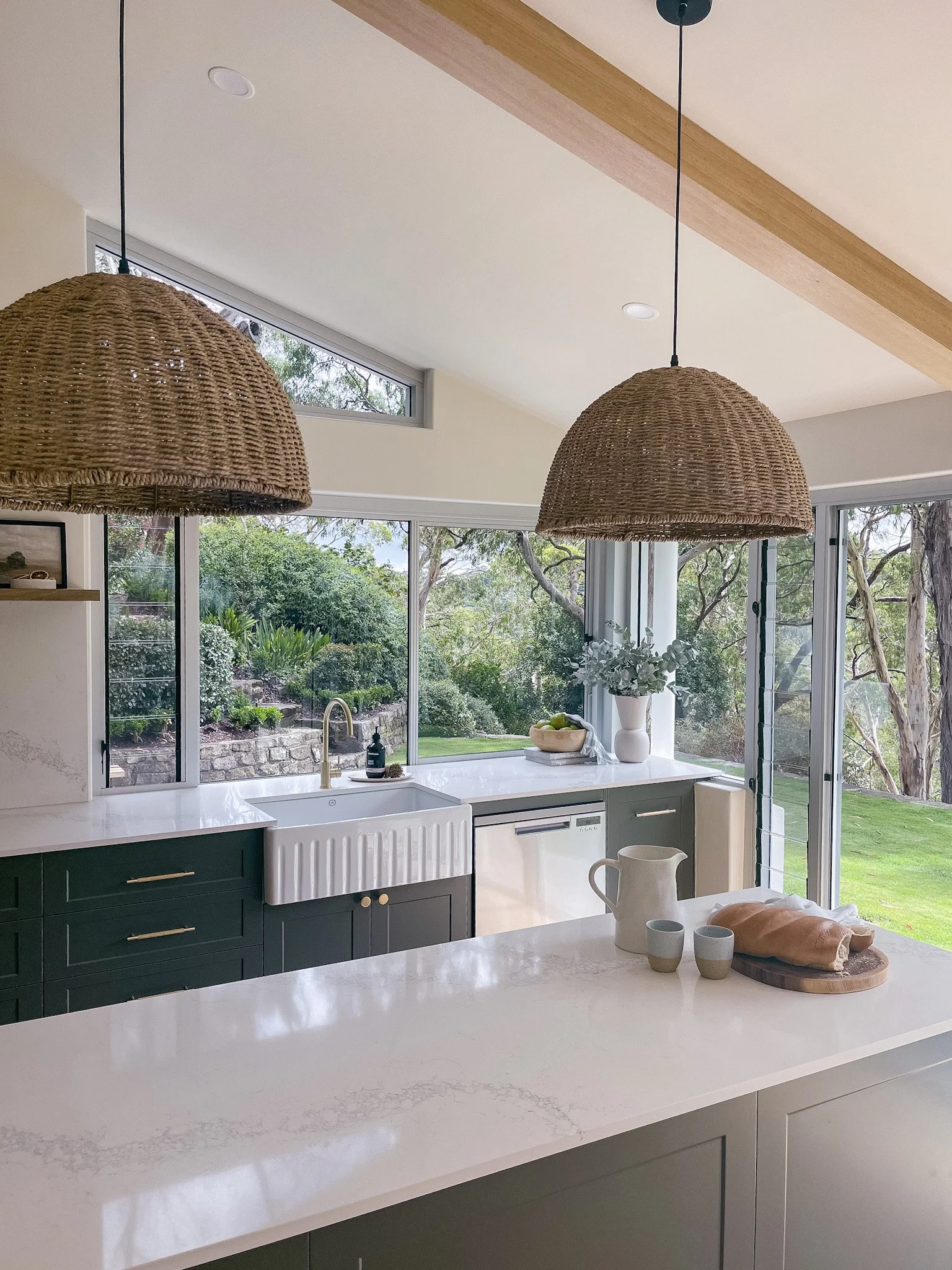Light-filled kitchen with woven pendant lights hung above a stone island bench, illustrating ideal pendant lighting height in a modern, natural interior.