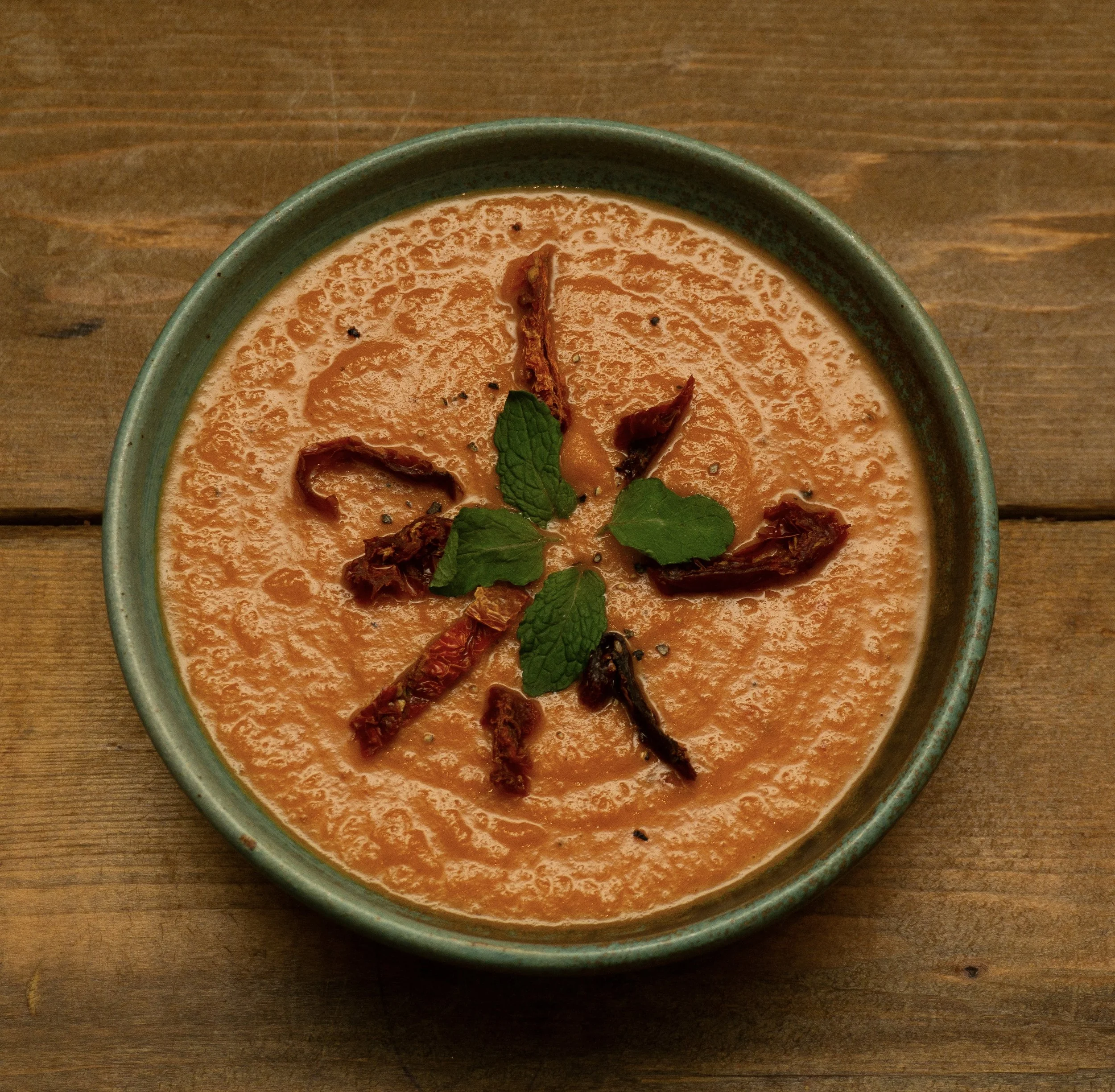 Creamy tomato bisque soup bisque topped with sun dried tomatoes, mint and black pepper in a handmade ceramic bowl.