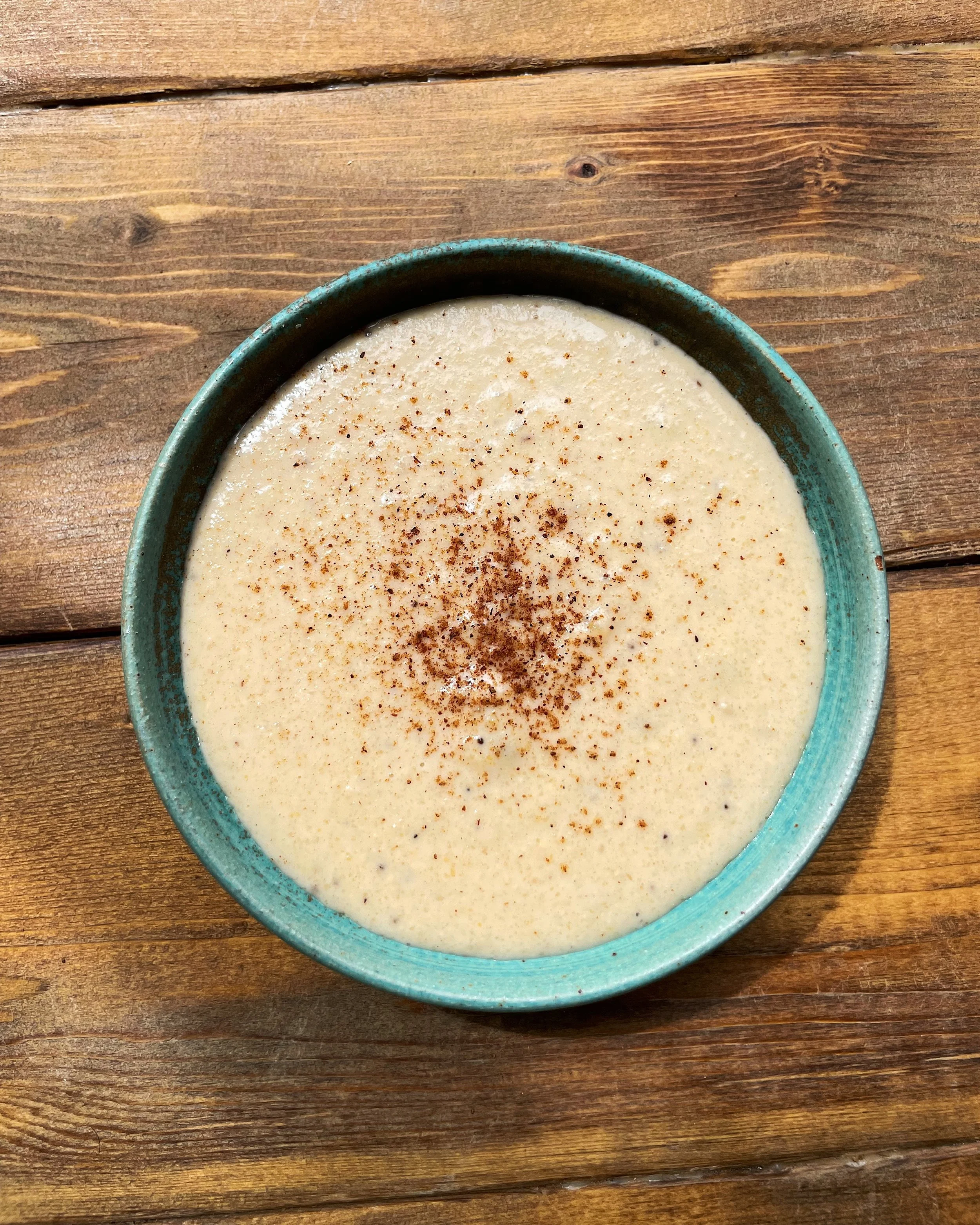 A bowl of green plantain porridge topped with sliced almonds and a sprinkle of cinnamon and nutmeg.