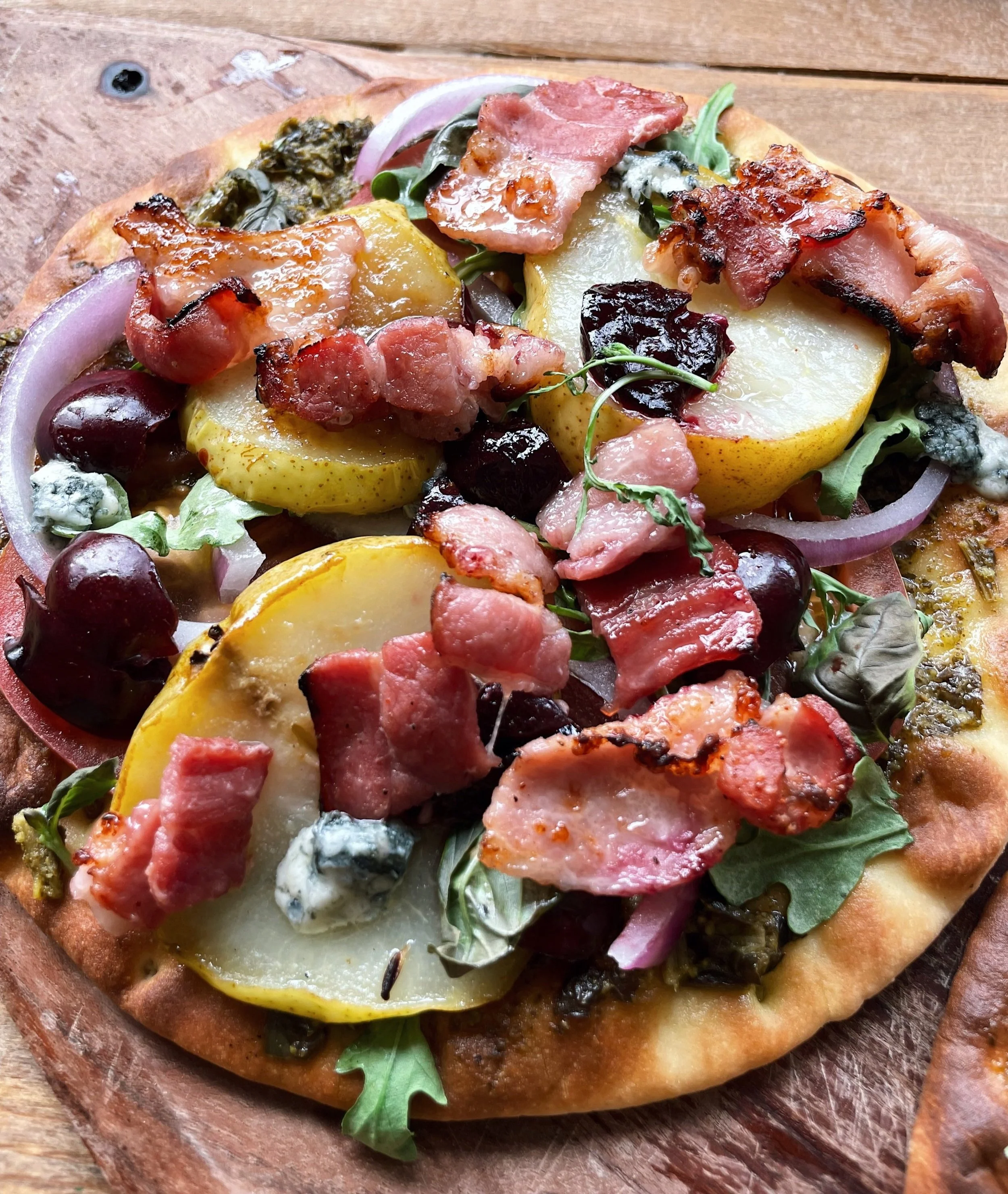 Sliced pear, bacon and gorgonzola pizza on a rustic wooden board, ready to serve.