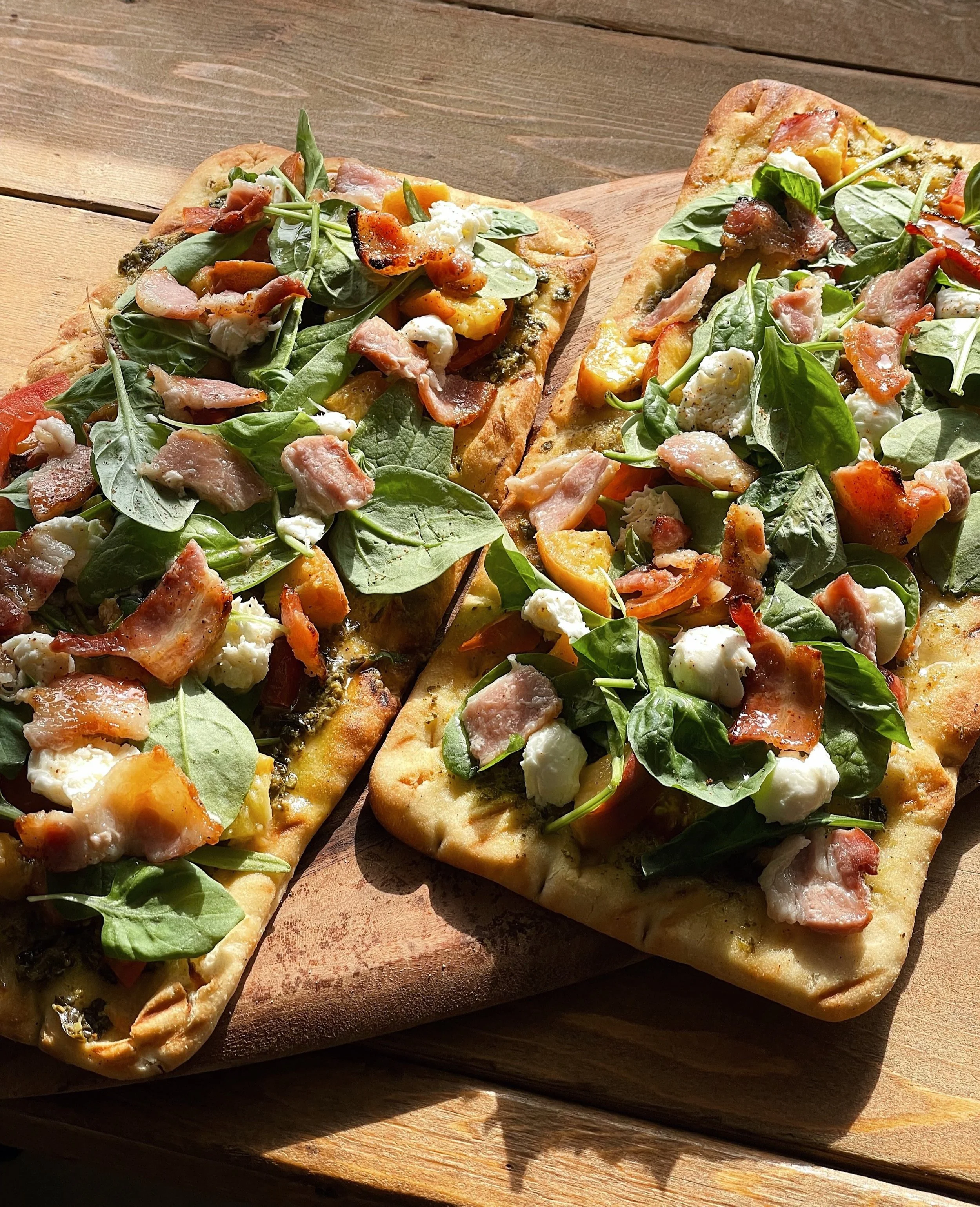 Golden-brown peach and pesto pizza garnished with fresh basil leaves, ready to serve