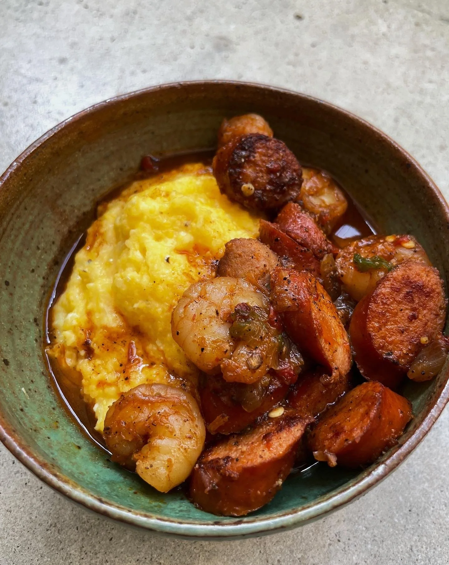 A ceramic bowl of Cajun shrimp, andouille sausage and creamy yellow grits.