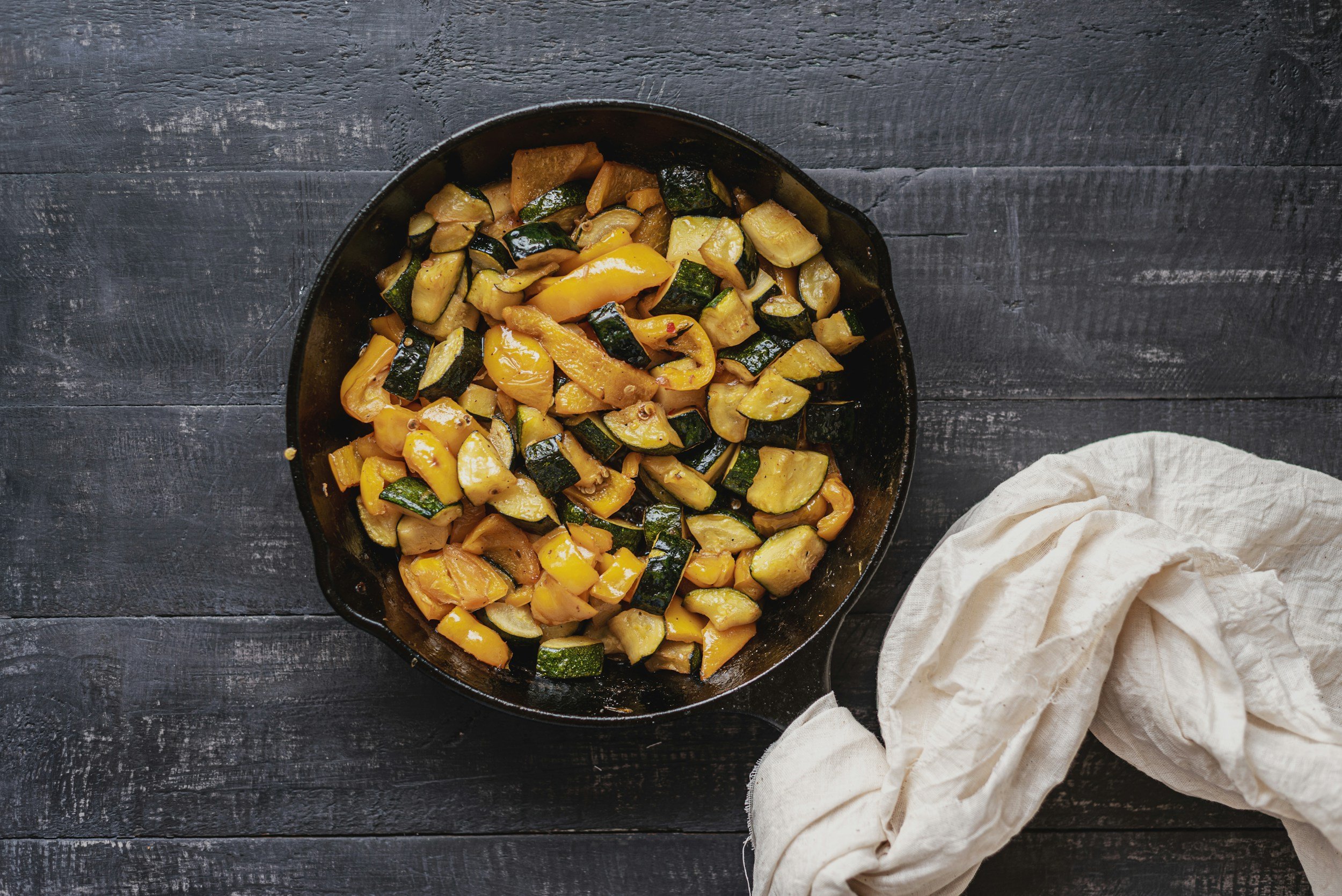 Cast iron skillet on a rustic wooden table, filled with freshly roasted zucchini and squash, showcasing the golden-brown texture of the vegetables.