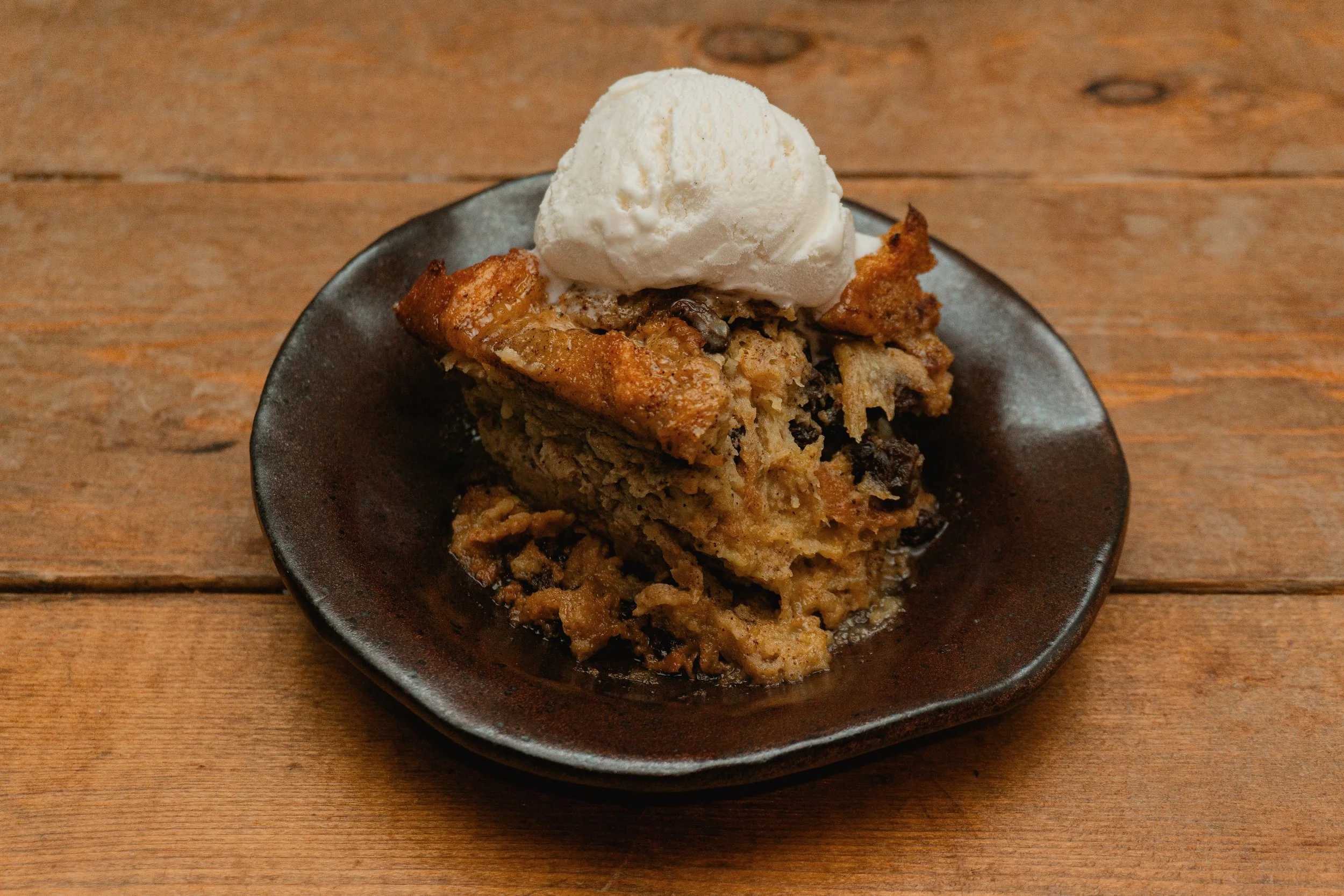 A slice of bread pudding with raisins topped with vanilla bean ice cream.