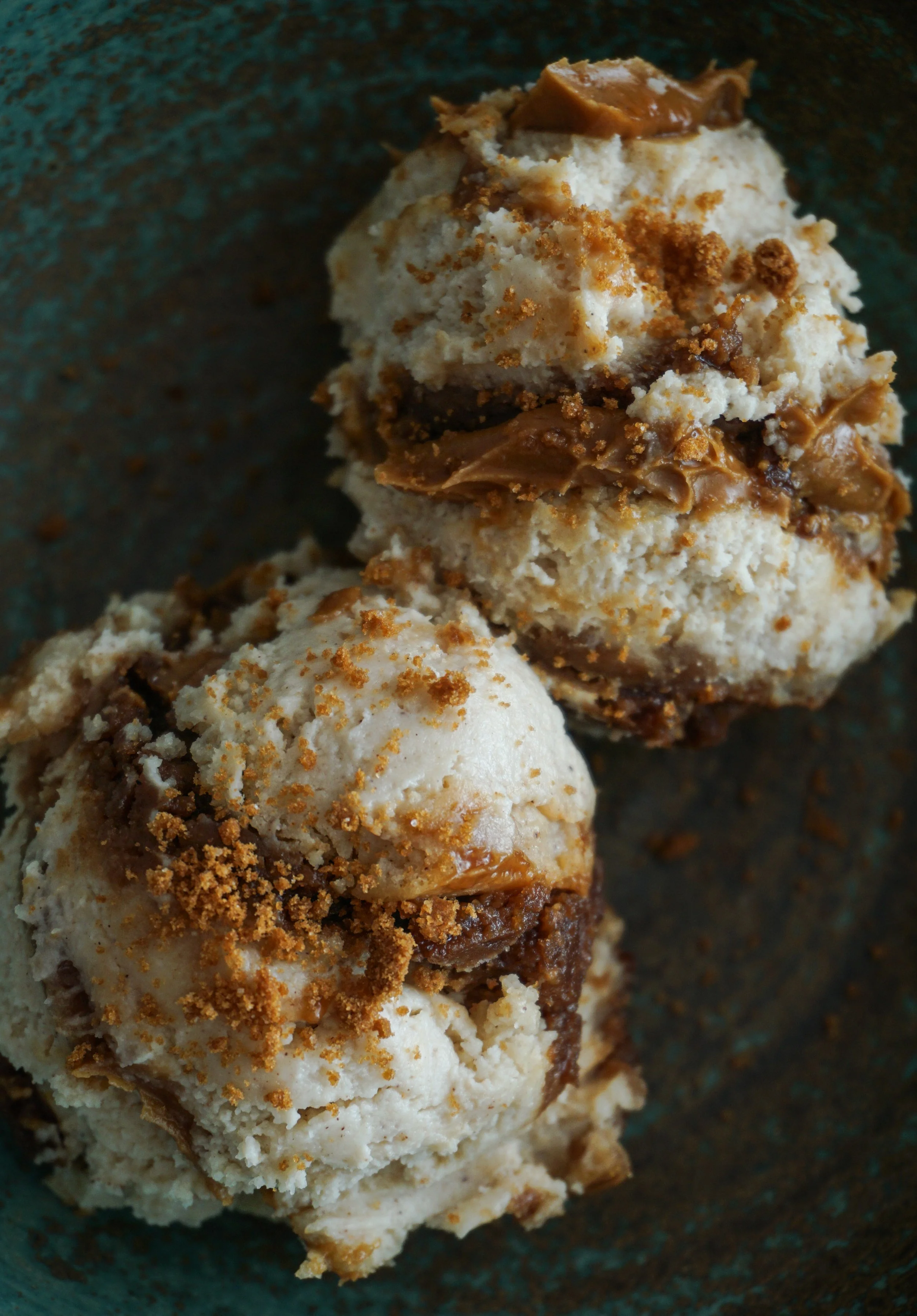 Close-up of two scoops of creamy Biscoff cheesecake in a rustic, handmade ceramic bowl, showcasing the smooth texture and warm golden tones of the spiced dessert.