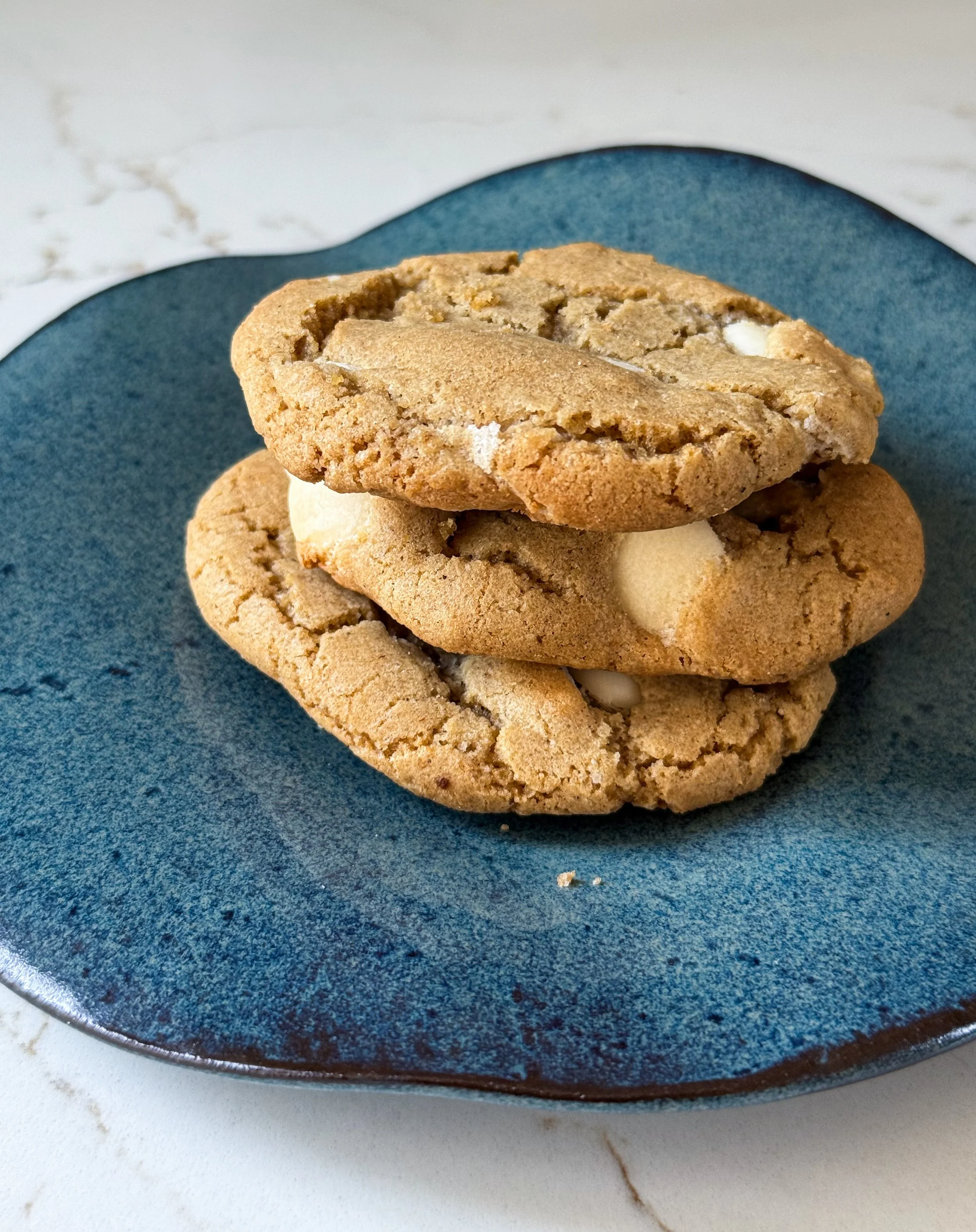 Soft, golden spiced white chocolate chip and marshmallow cookies served on a handmade blue ceramic plate, with gooey marshmallow pockets and melted white chocolate visible on top.