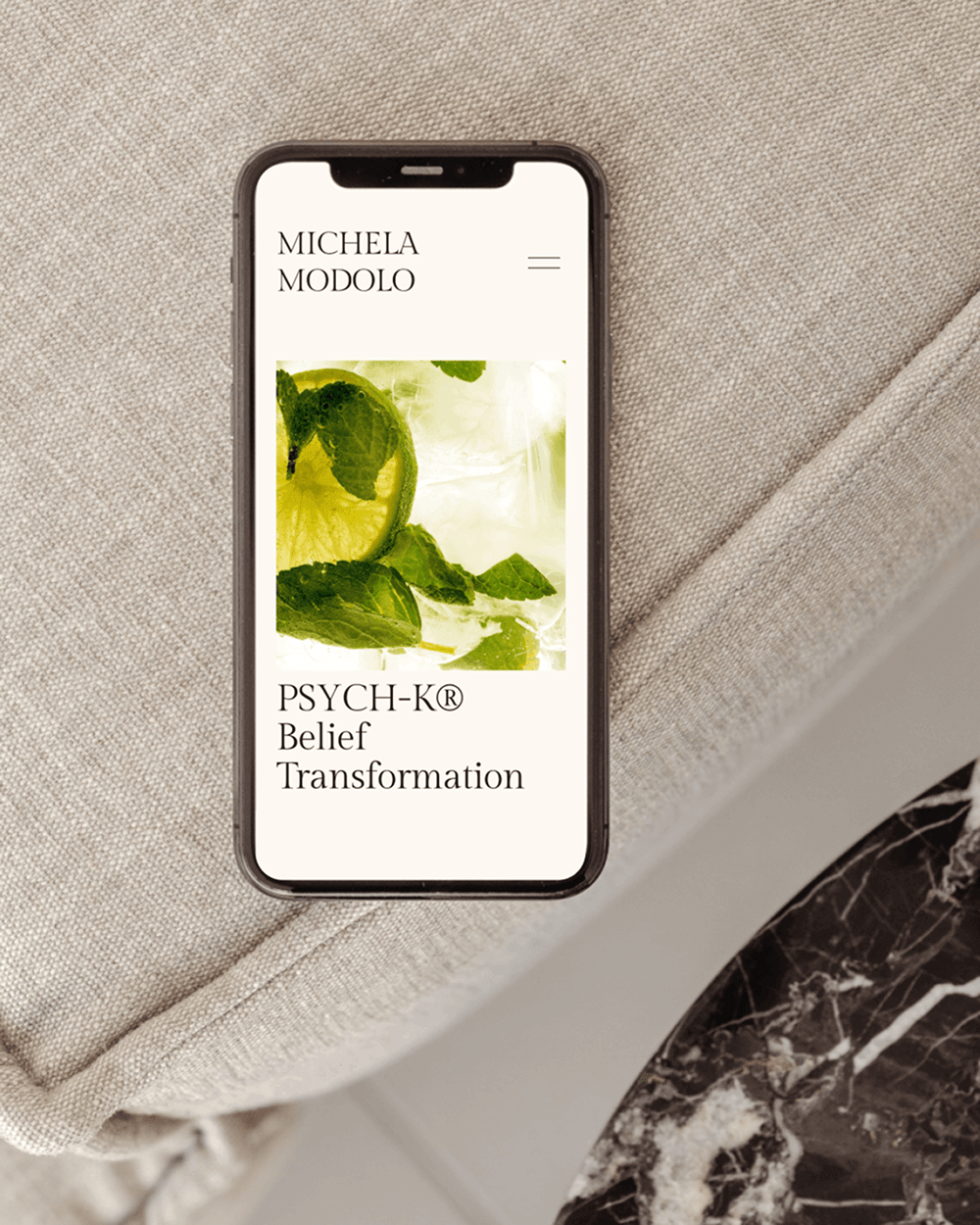 Smartphone displaying the website of Michela Modolo with an image of lime slices and mint leaves and text about belief transformation.