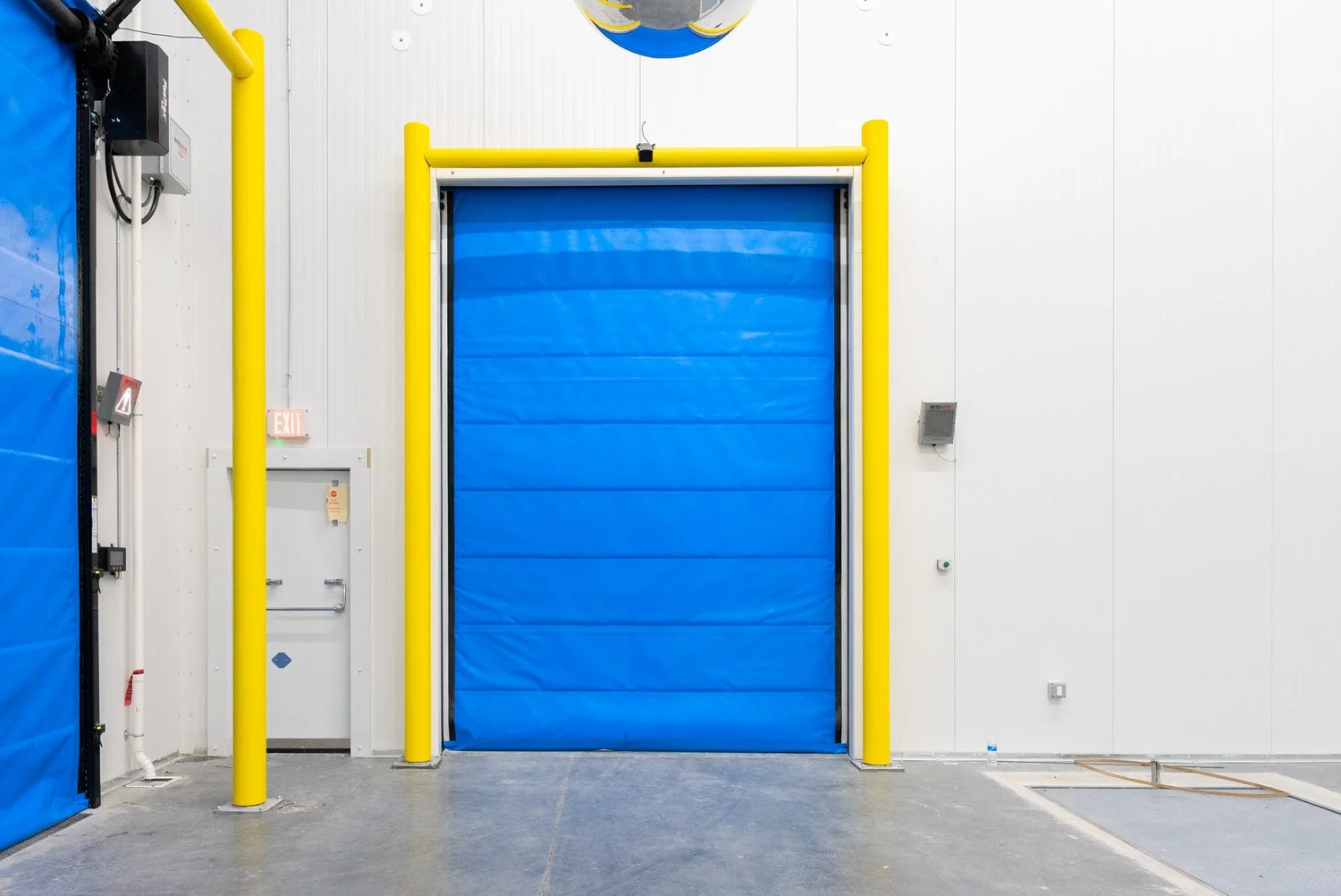 Blue insulated cold storage door framed in yellow in a white panel wall