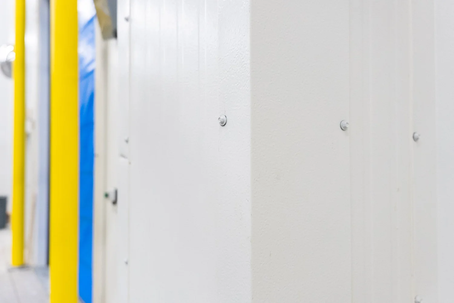 Close-up of white insulated metal panel walls beside a yellow door frame