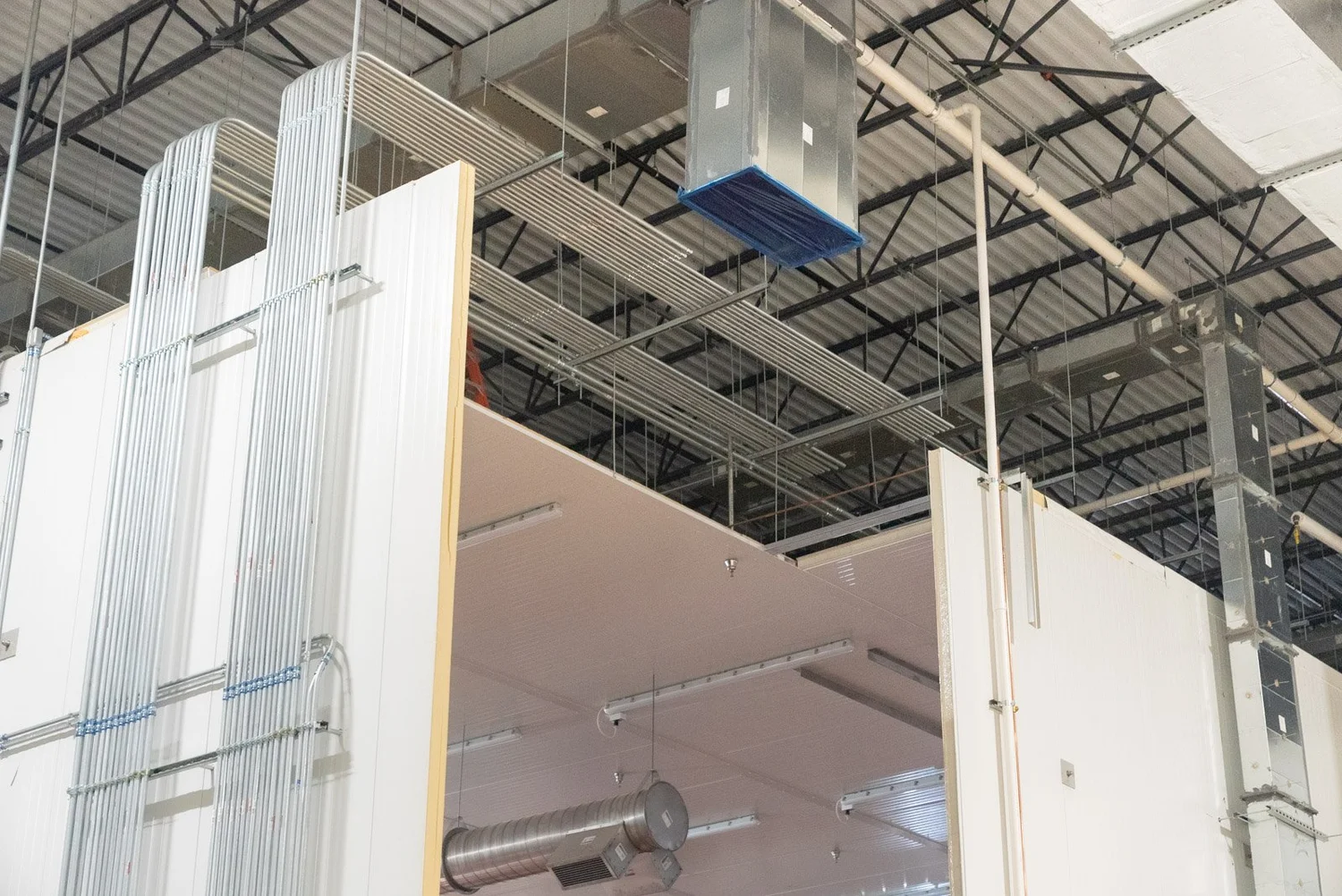 Insulated metal wall panels being installed beneath the roof structure of a warehouse