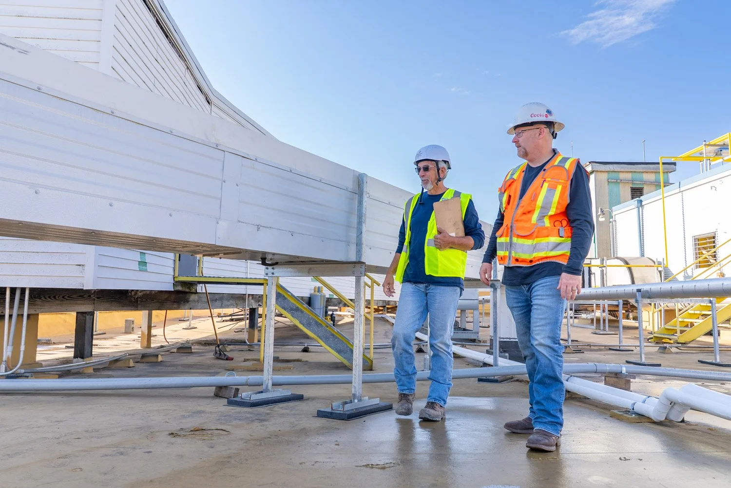Two crew members in hard hats walking beside rooftop insulated metal panel ductwork