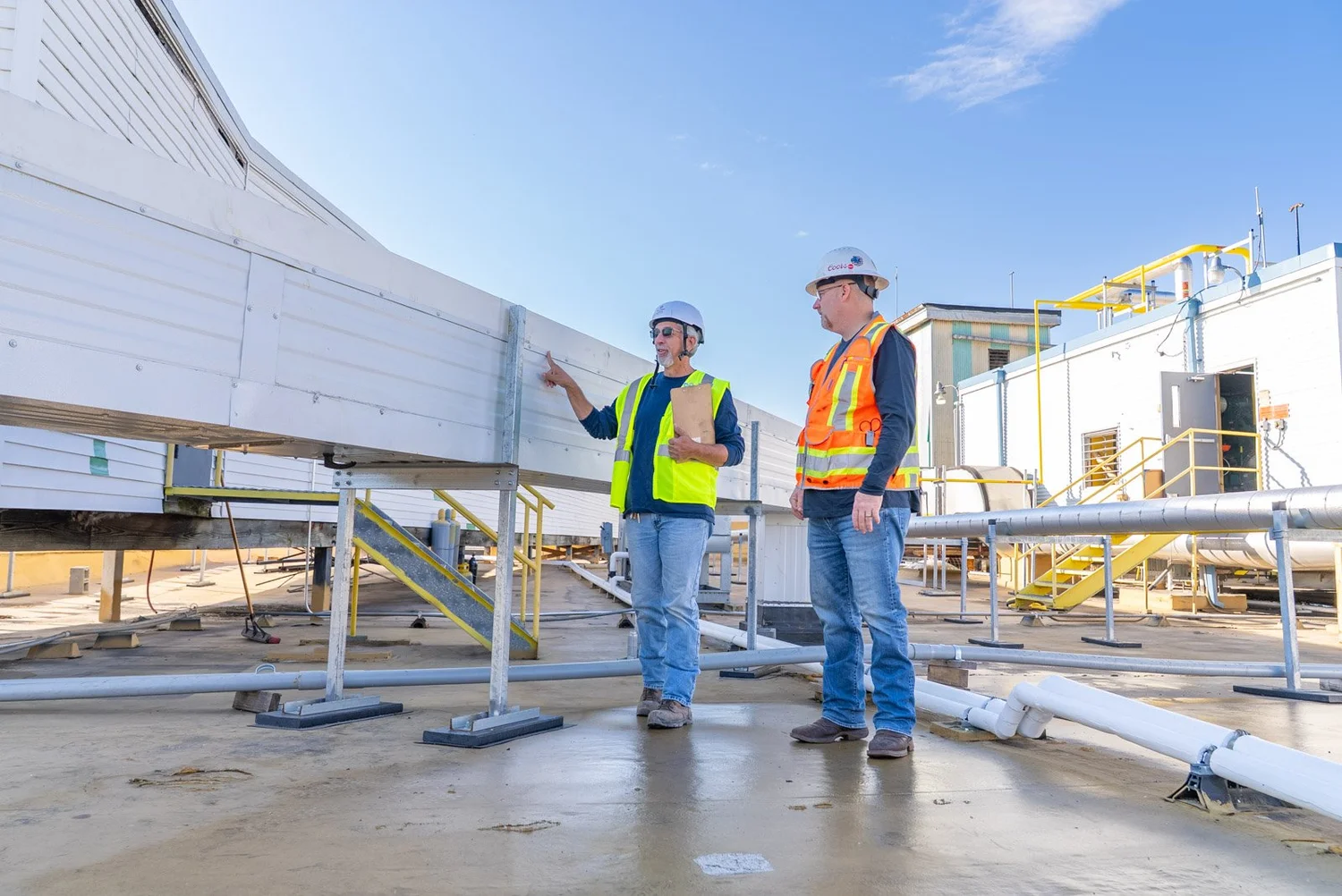 Two crew members in hard hats beside a rooftop insulated metal panel duct system