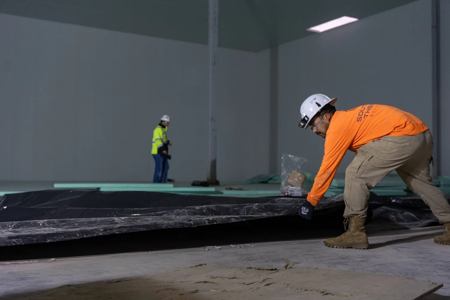 Crew member laying insulation boards across a large floor with a second worker behind