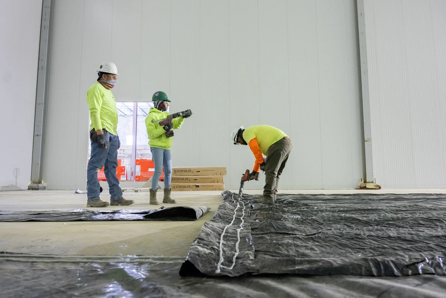 Crew members installing insulation and vapor barrier on the floor of a cold storage room