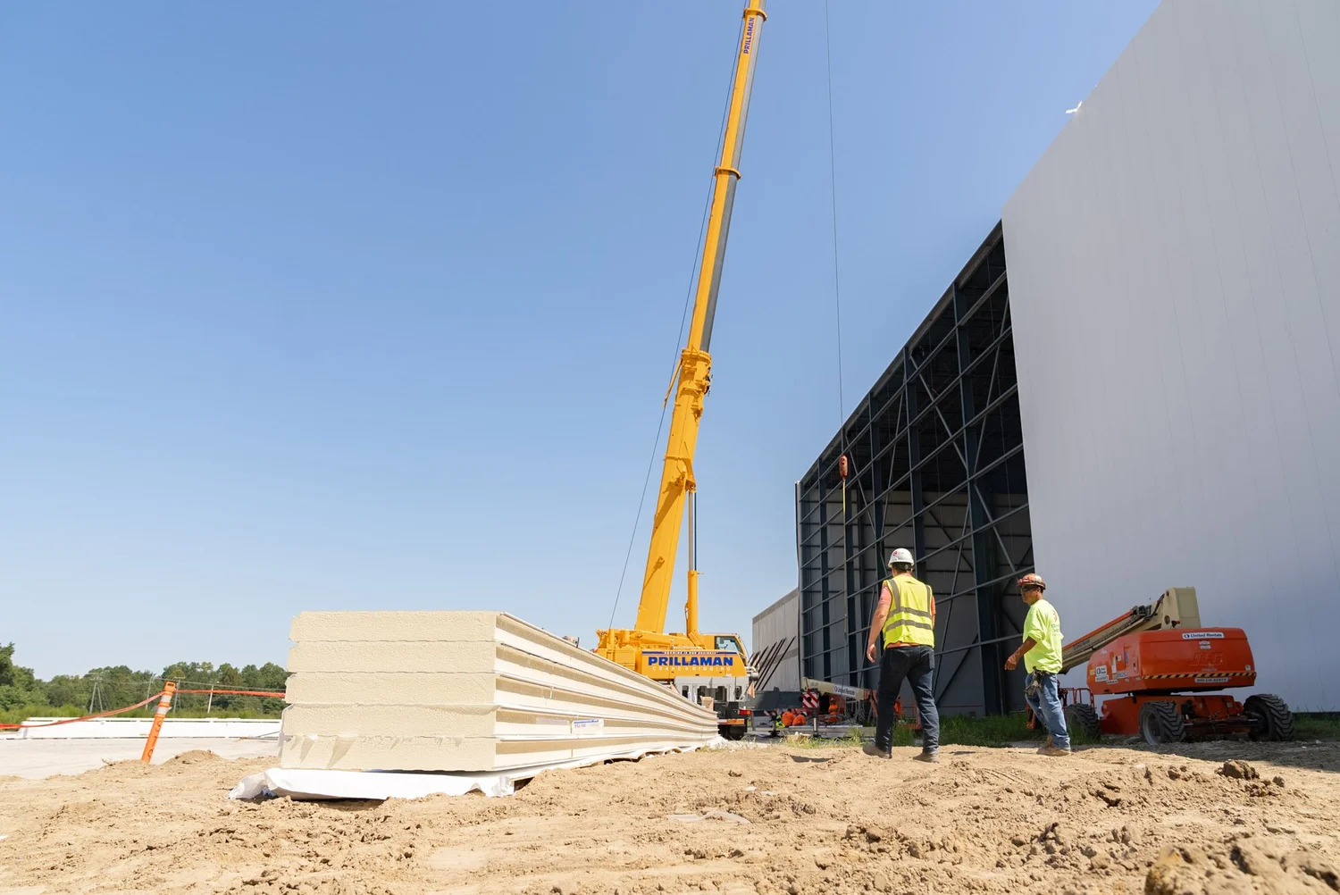 Crane lifting an insulated metal panel onto a tall building exterior as crew members watch