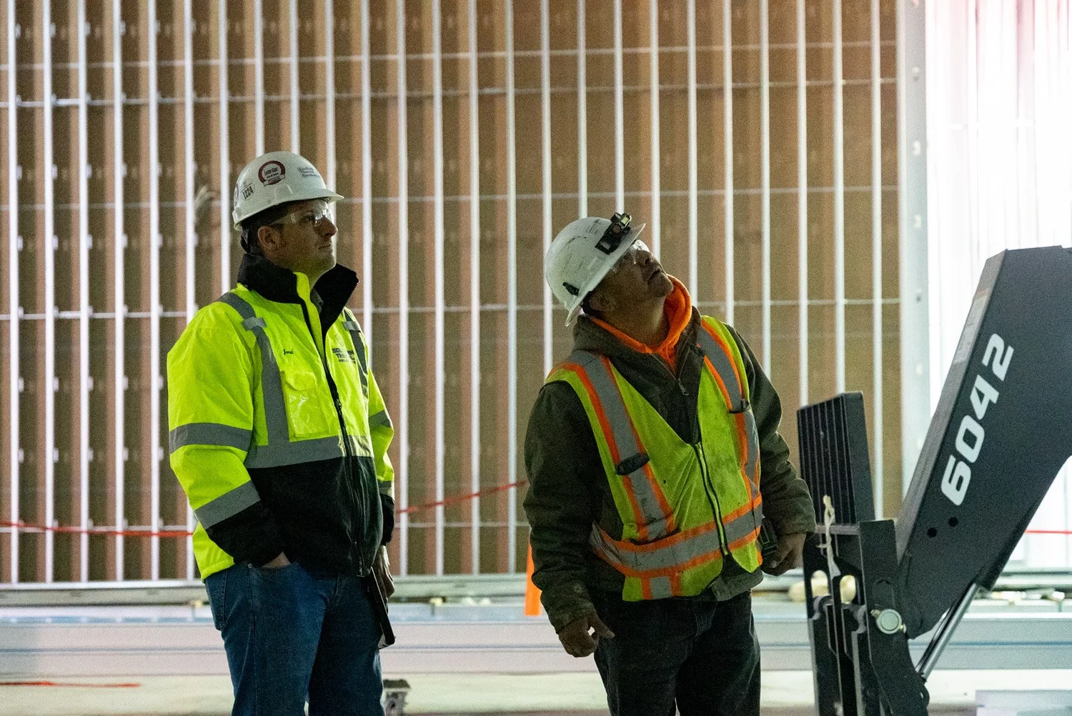 Two crew members in hard hats and safety vests inspecting work beside a lift