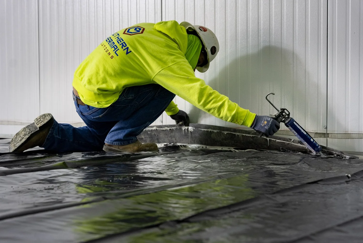 Crew member in a Southern Thermal Solutions jacket sealing a floor seam